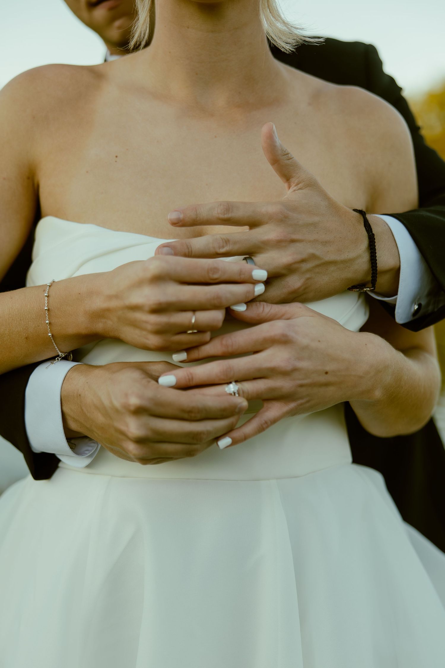 Close-up shots of hands displaying wedding rings against a white wedding dress.