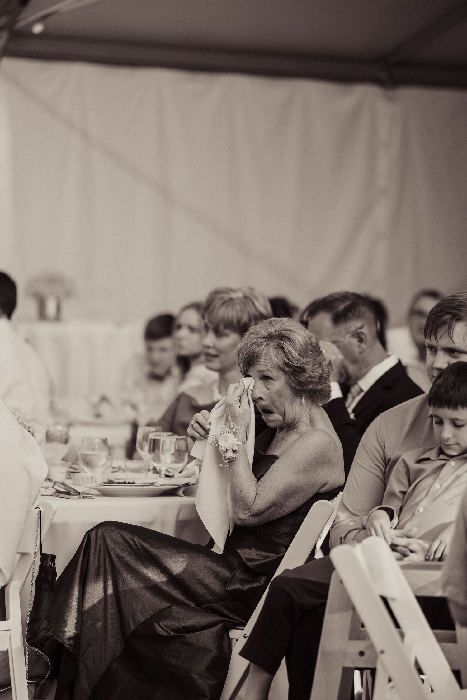 Black and white photo of wedding reception guests seated at tables during emotional moment.