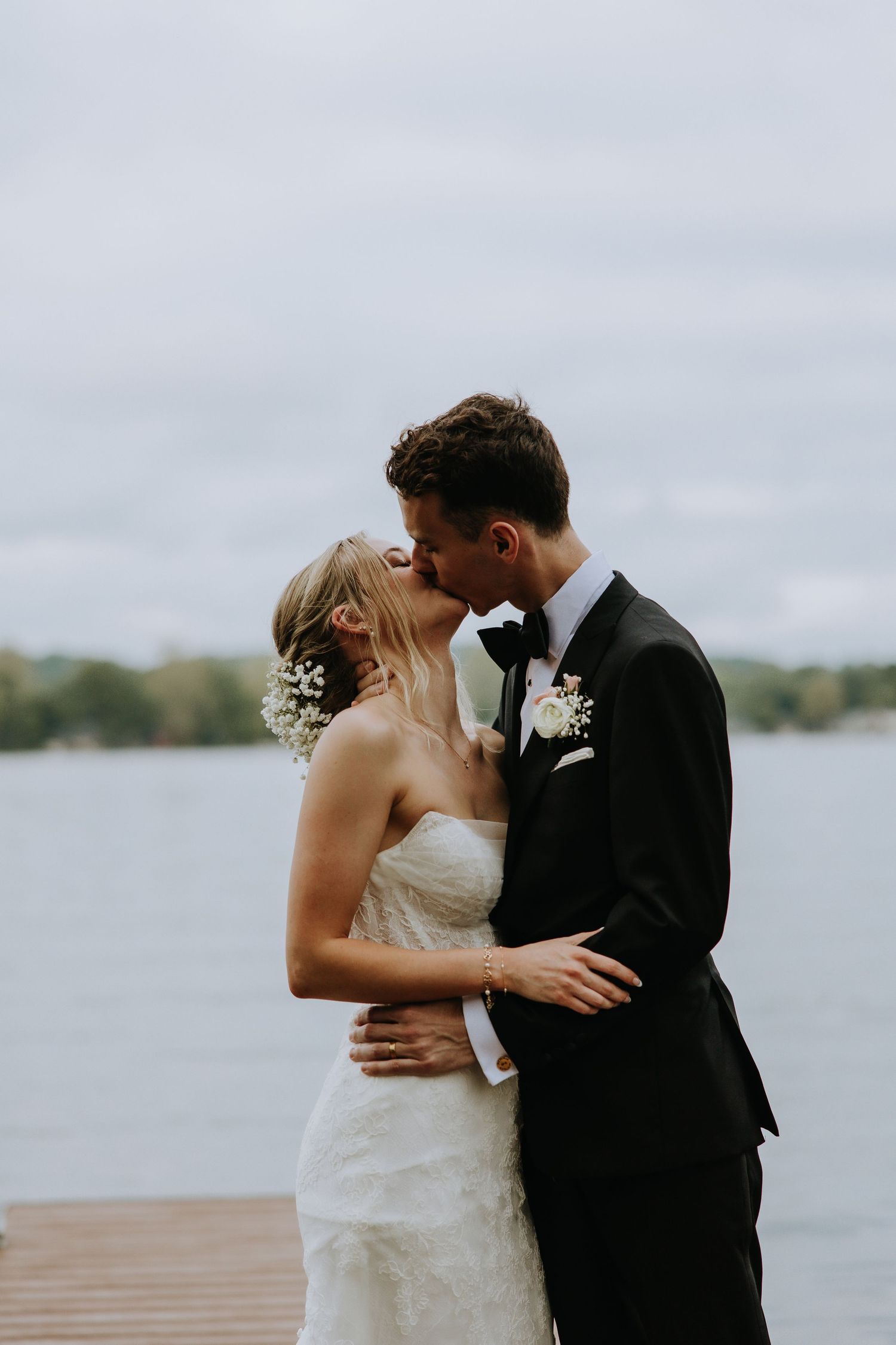 A romantic wedding couple shares intimate moments on a dock by a serene lake.