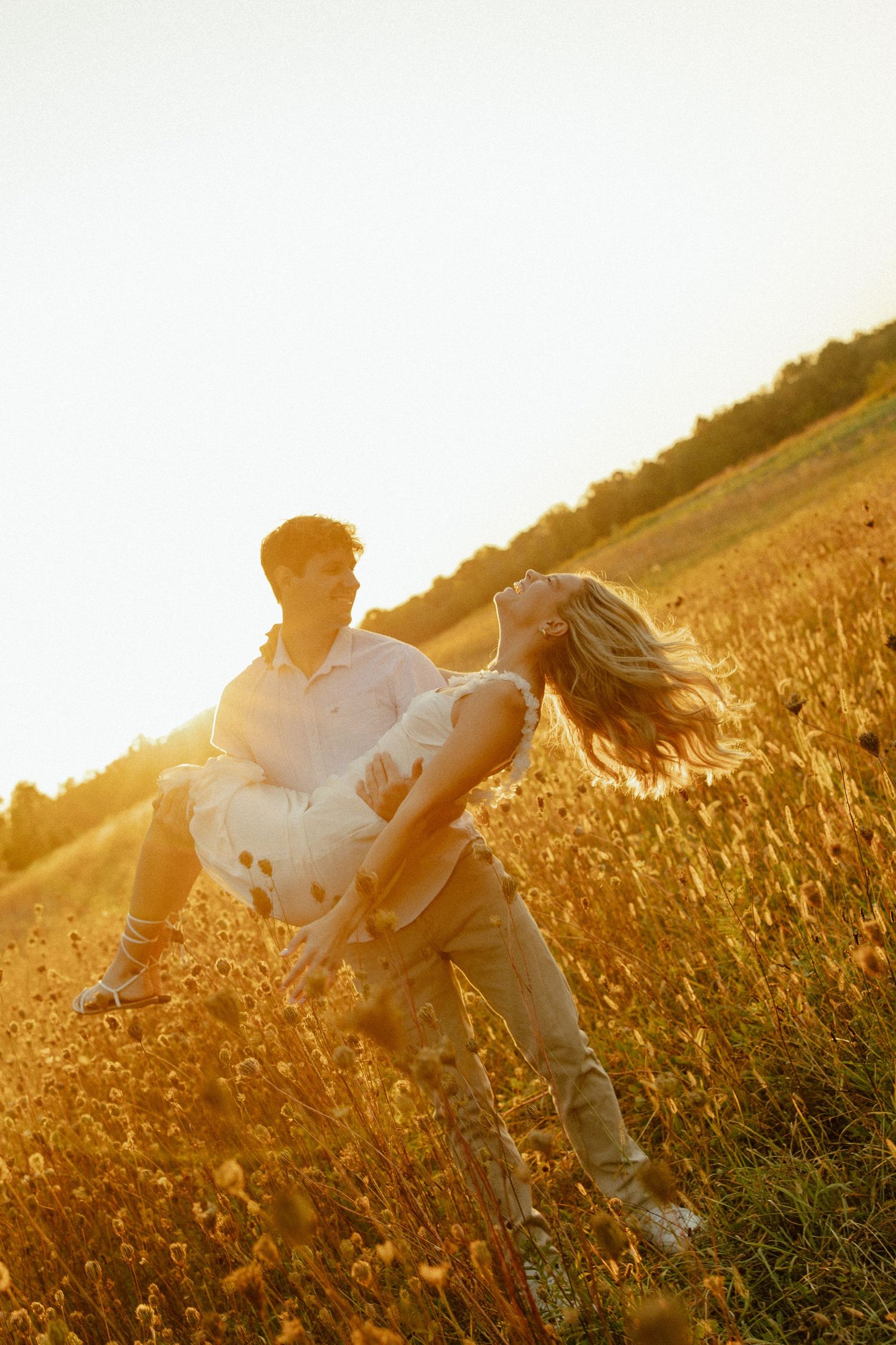 A couple embraces in a golden wheat field during sunset creating a romantic silhouette against the warm light.