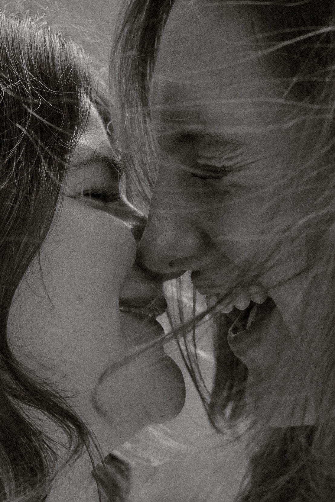 A black and white close-up portrait of two people sharing an intimate moment with joyful expressions.