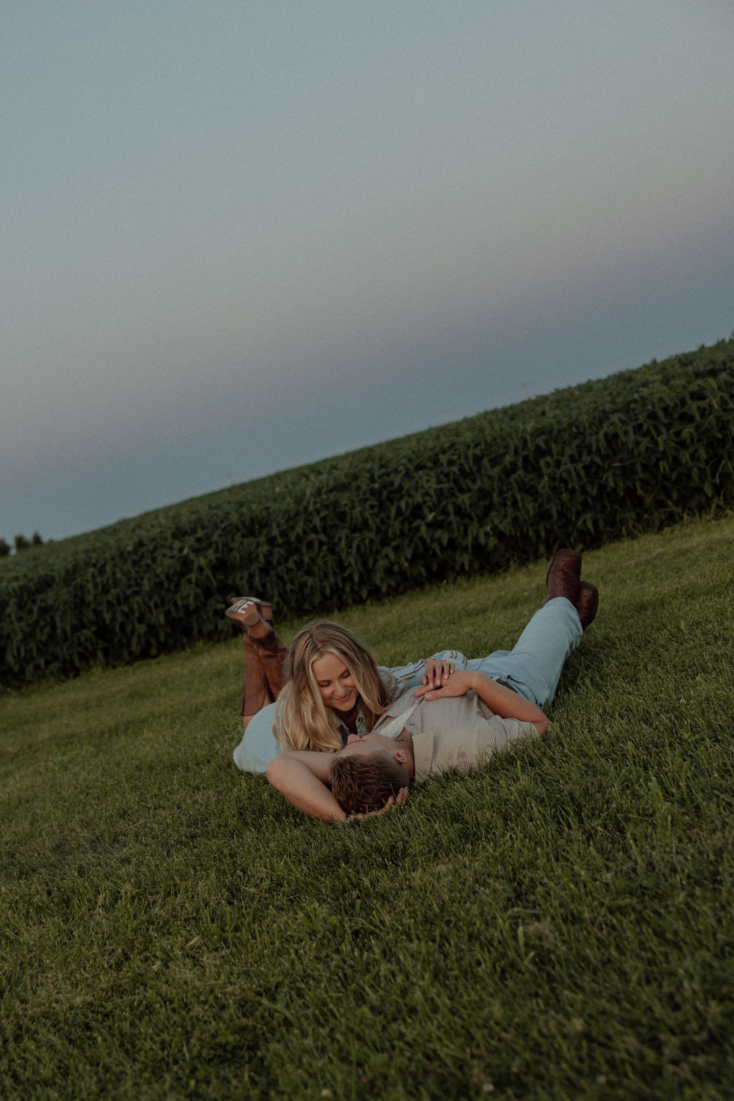 A couple lying together on a grassy hillside during sunset, creating a romantic outdoor moment.