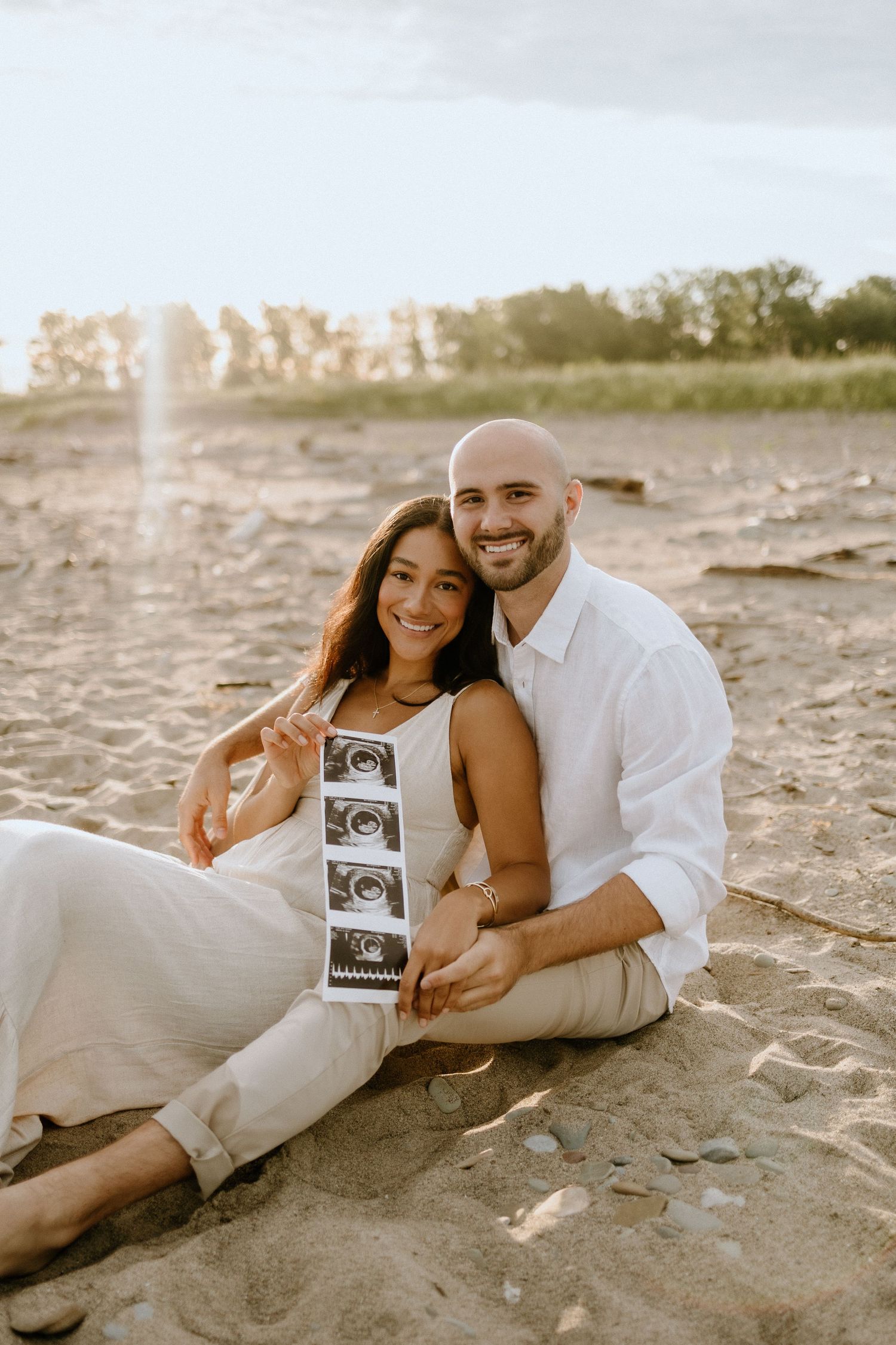 Happy couple shares ultrasound photos during beach maternity session at golden hour.