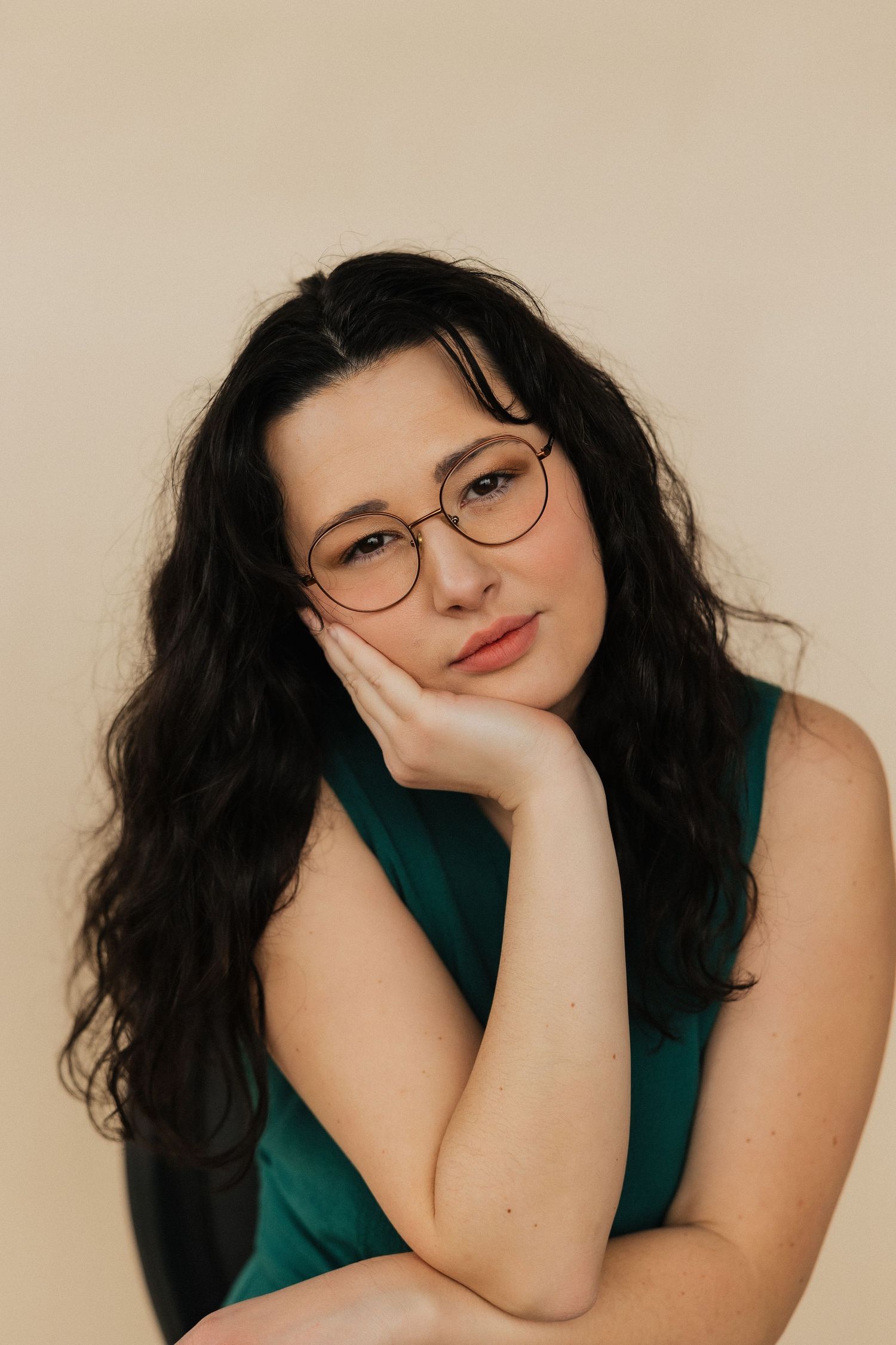 Close-up portrait of person in green top and glasses against beige background.