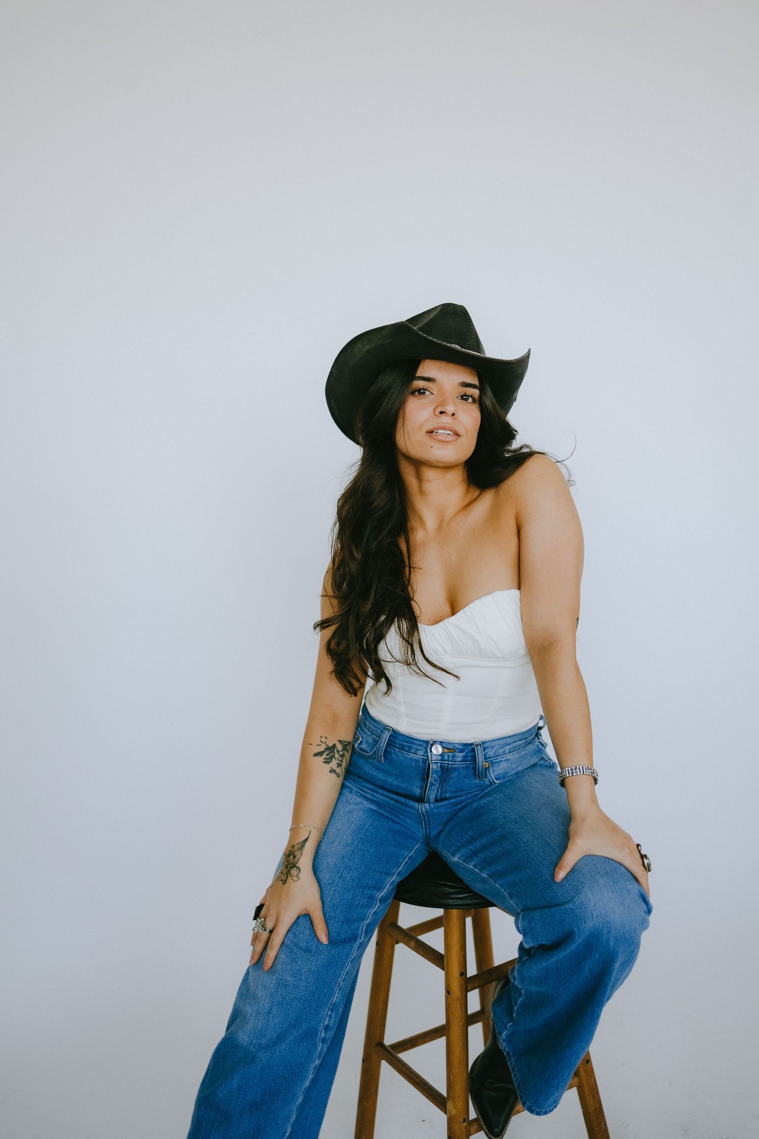 Western-inspired portrait with white top, blue jeans and black cowboy hat against grey backdrop.