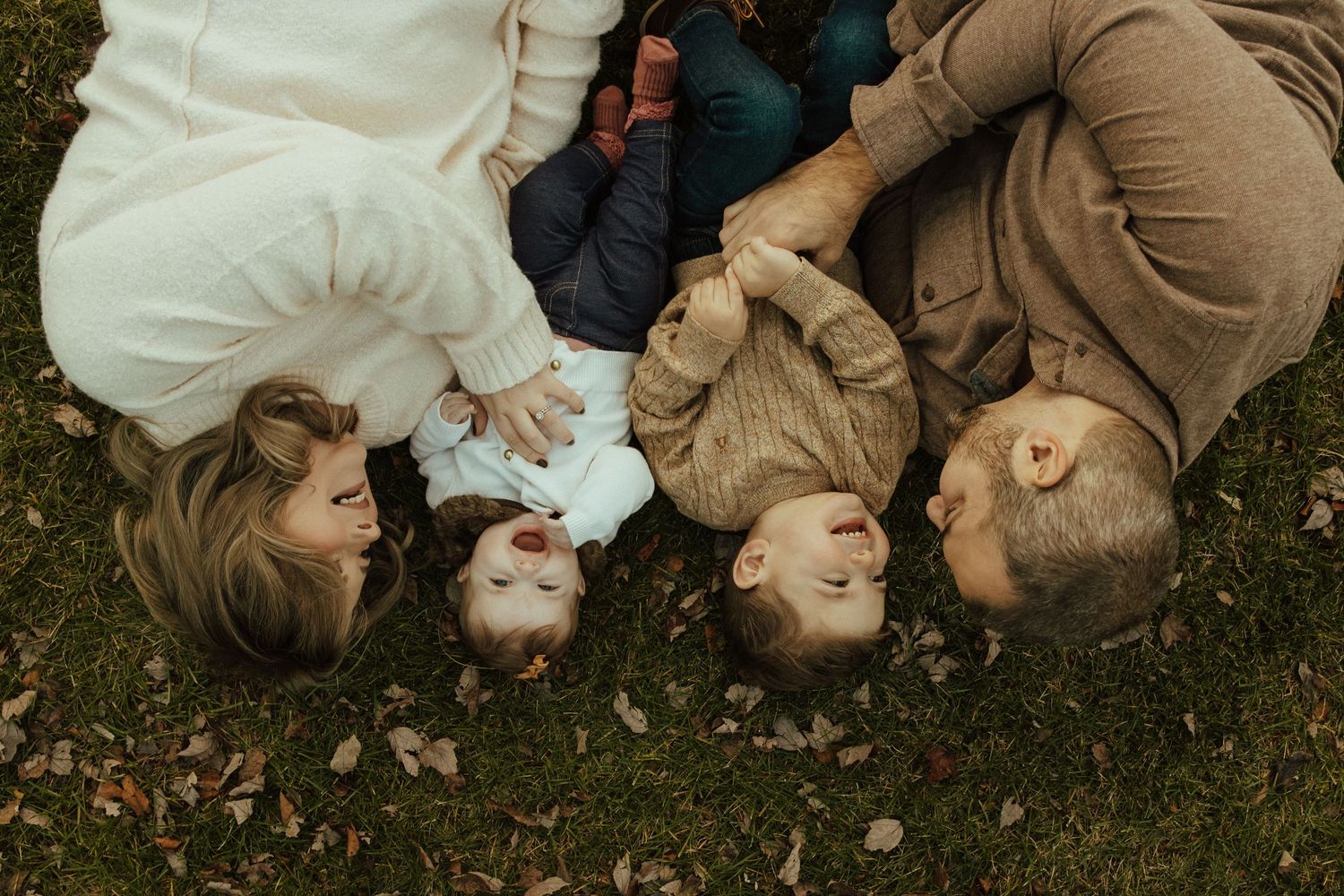 Group of people lying on grass in a circle formation with heads together creating a playful outdoor moment.