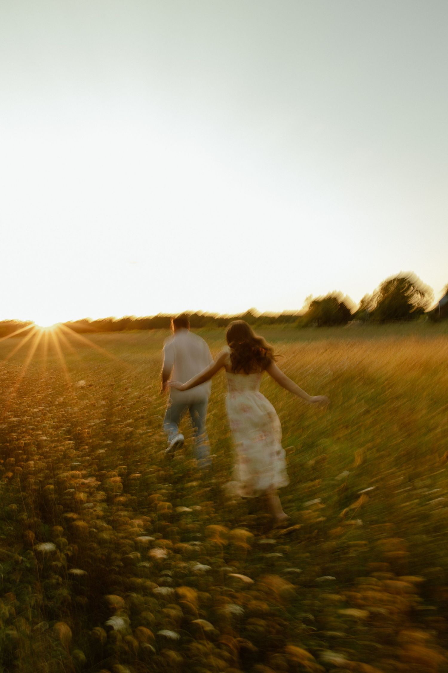 A couple walks through a sunlit field at golden hour as sunbeams create a dreamy atmosphere in the countryside.