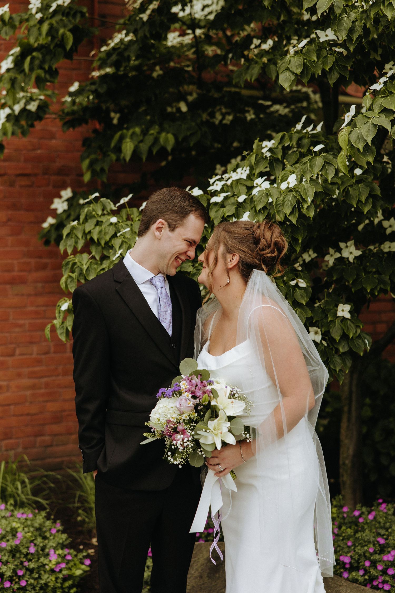 Romantic wedding couple sharing intimate moments against a brick wall with greenery.