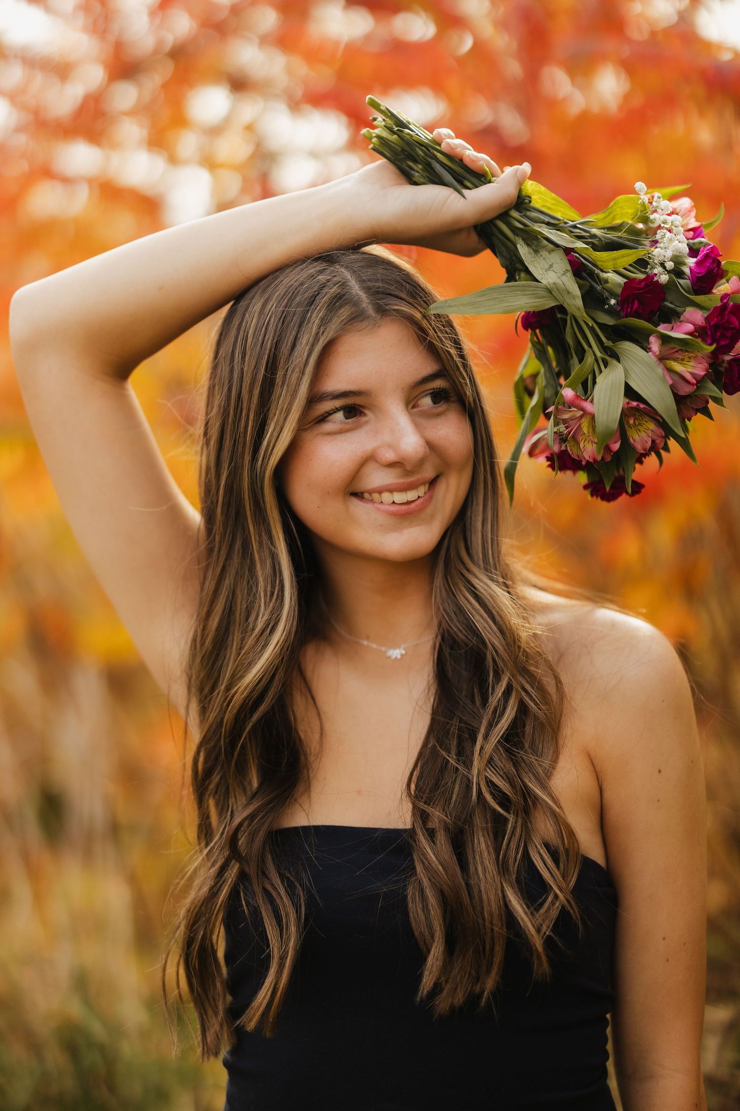 A casual portrait with flowers held overhead against warm autumn bokeh.
