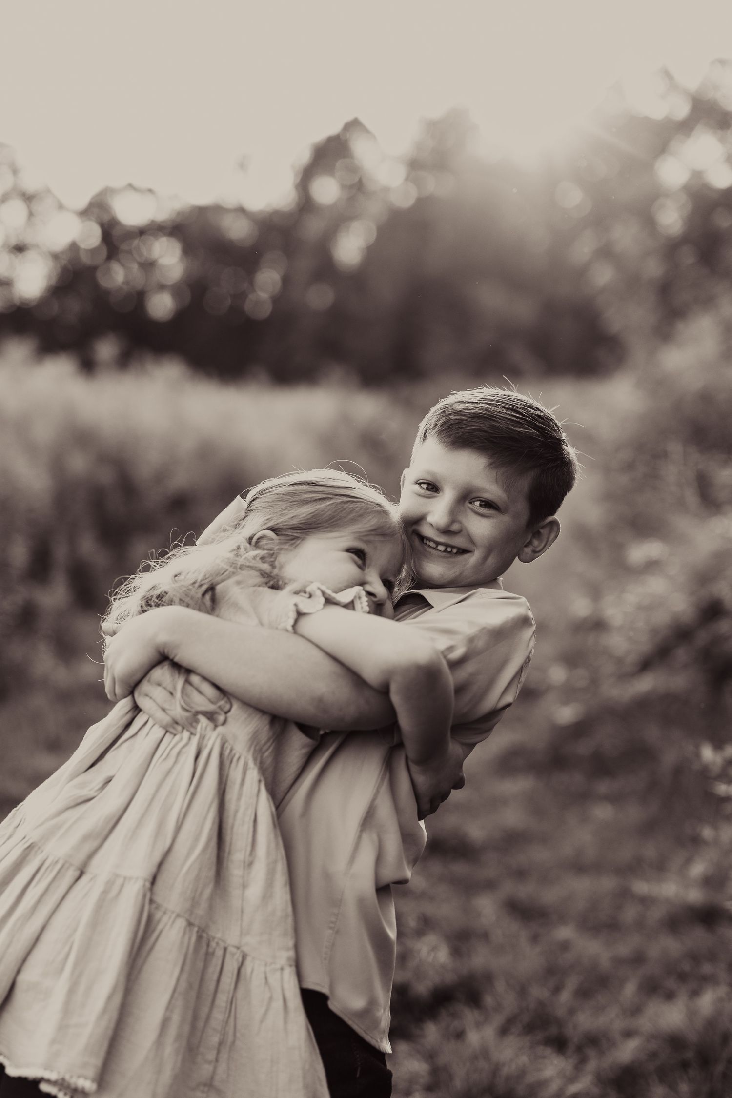 Two children share a sweet embrace in black and white portrait.
