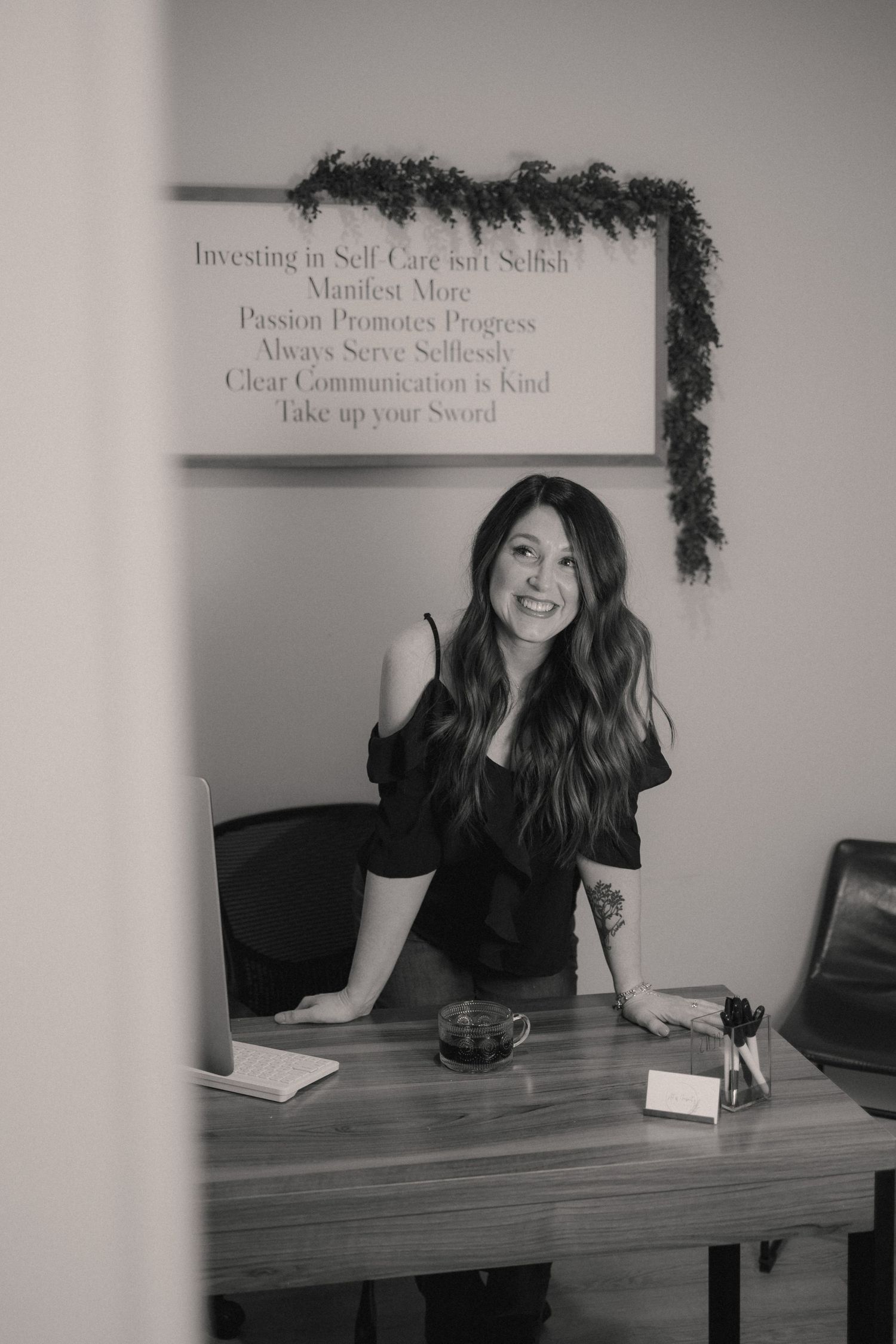 Person in black top sits at desk with decorative garland and text on wall behind.