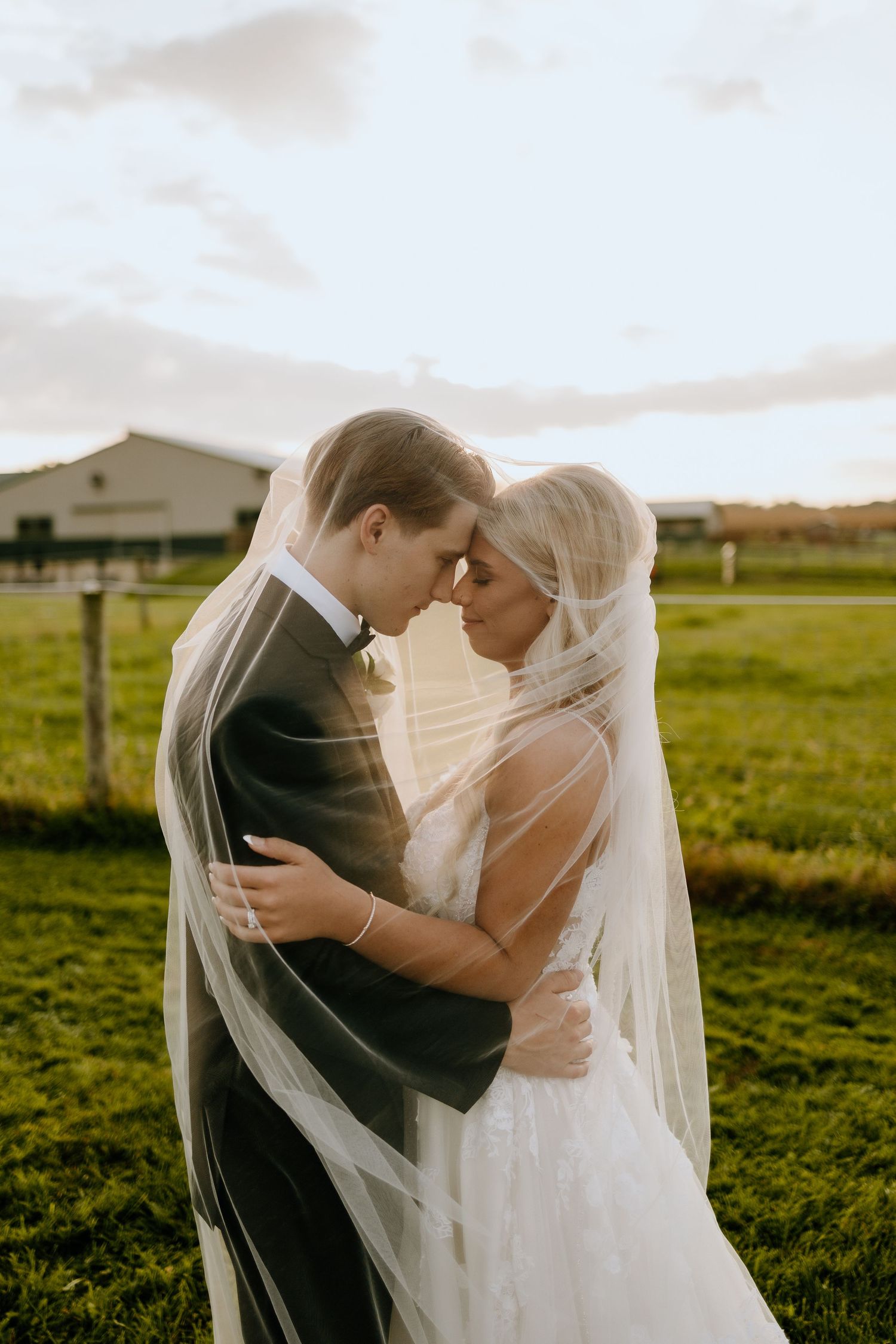 Romantic wedding photography captures a tender moment between newlyweds embracing in a sunlit field at sunset.