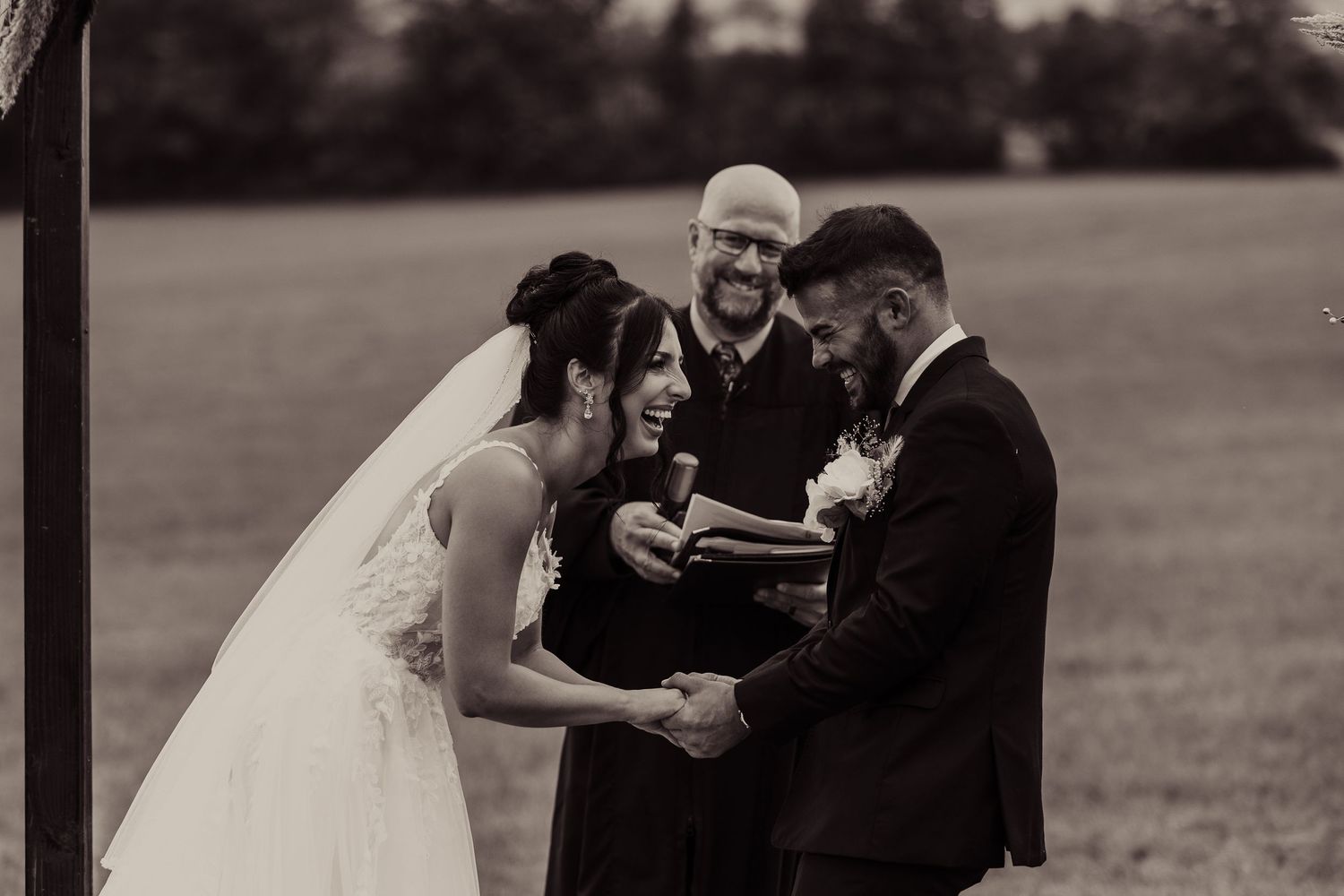 Black and white photo of wedding ceremony with couple and officiant in outdoor setting.