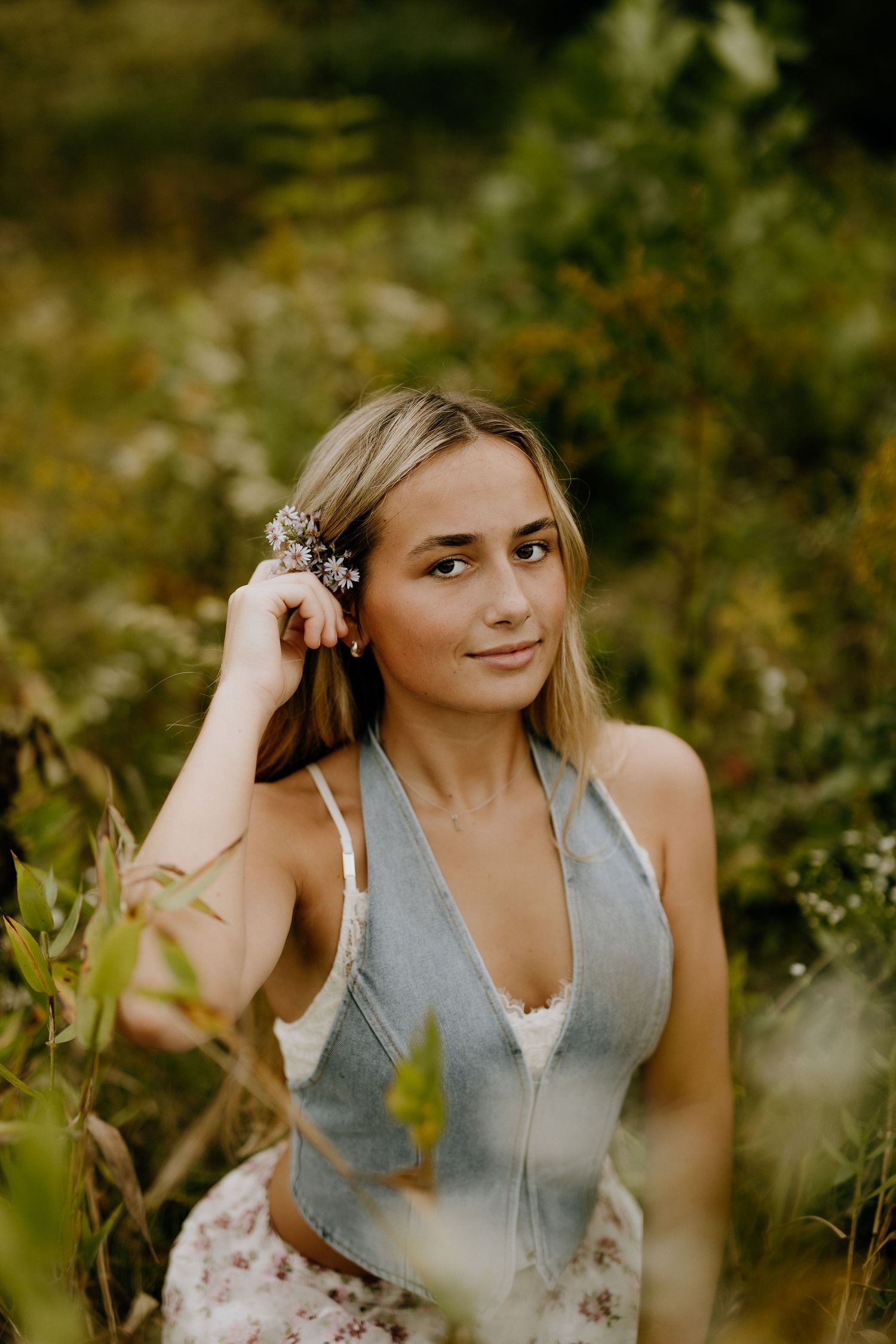 Dreamy portrait in meadow wearing gray top with delicate dried flowers in hair.