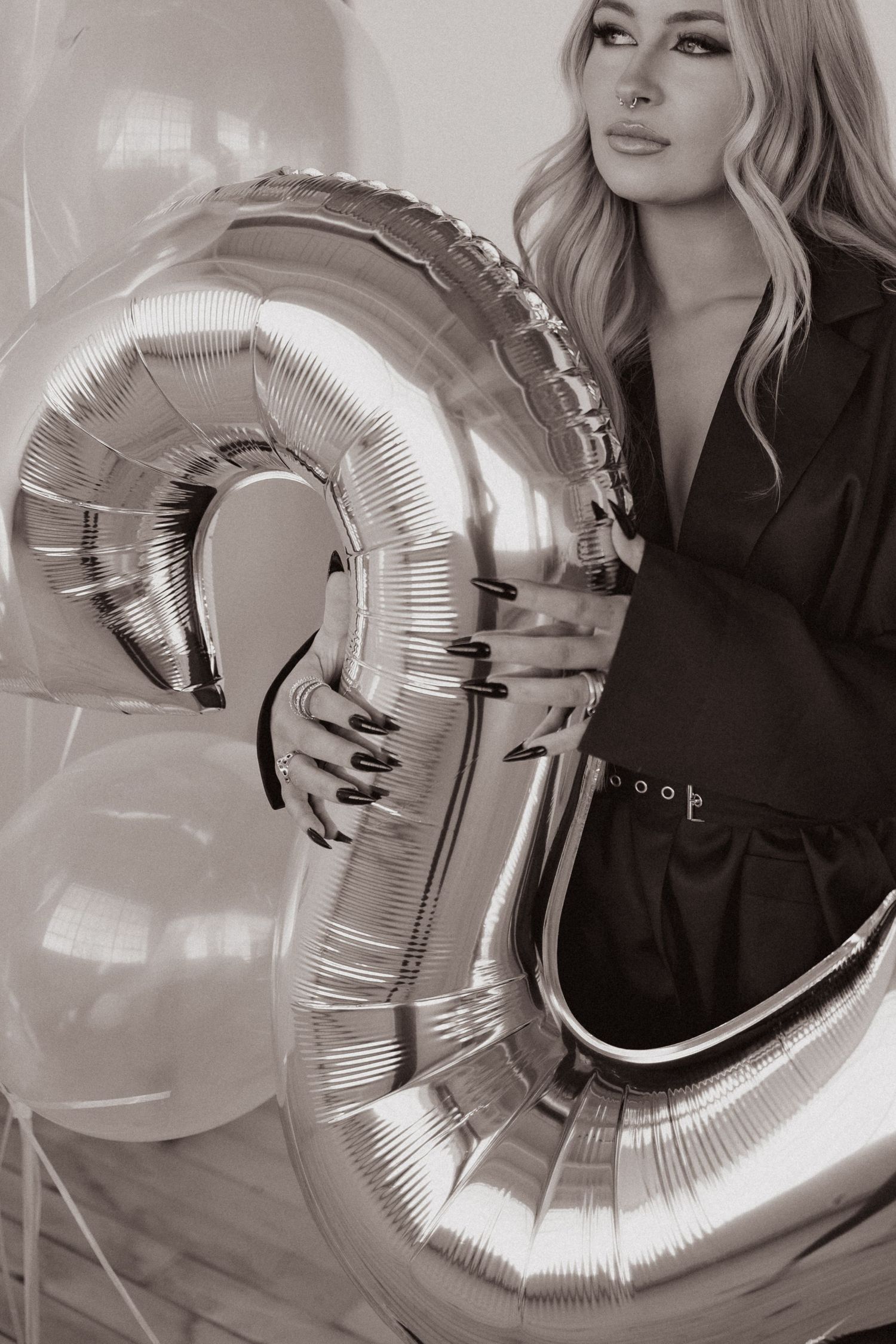 Black and white photo of person holding large silver number balloon with decorative balloons.
