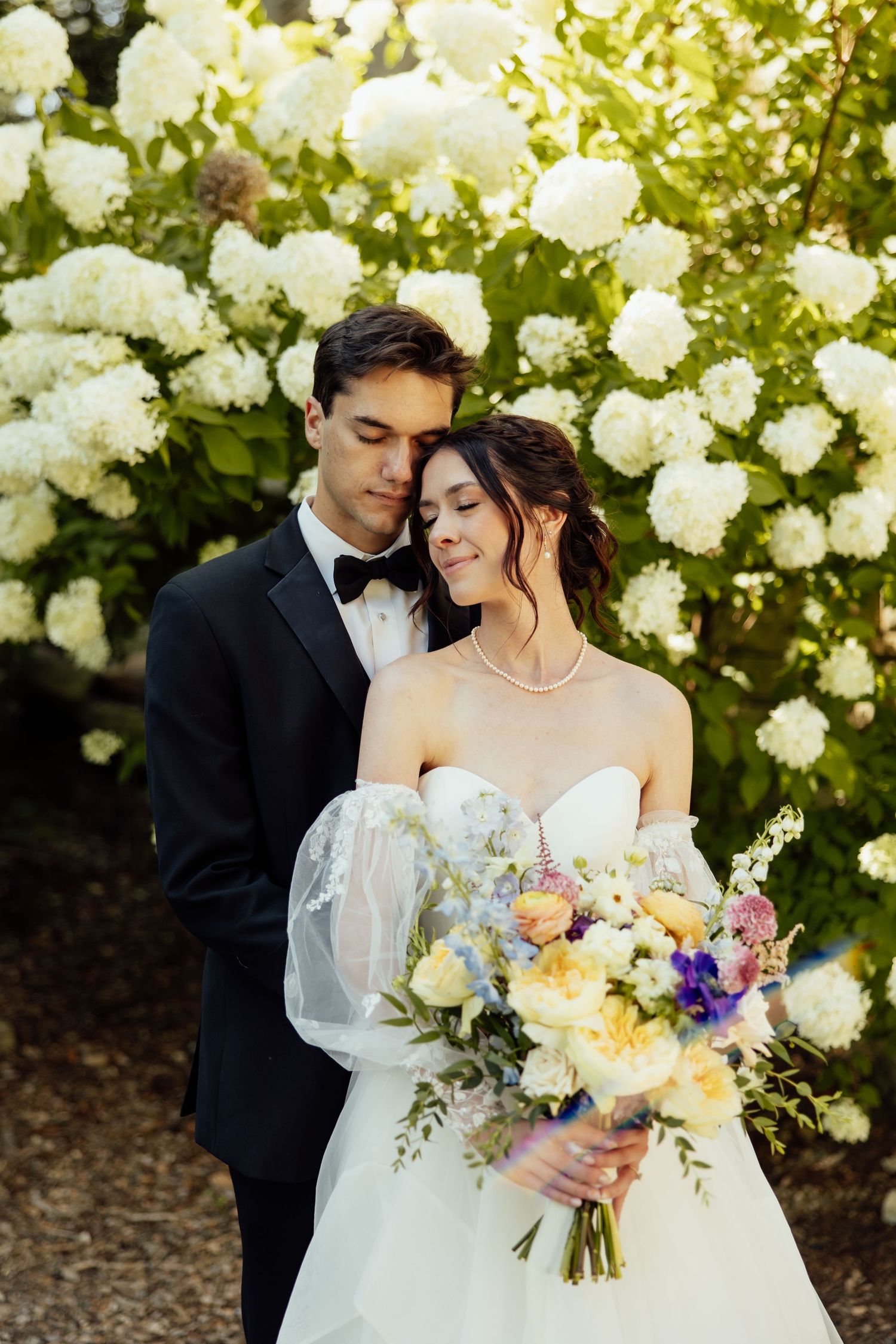 A romantic wedding portrait with white hydrangeas and a colorful spring bouquet in the garden.