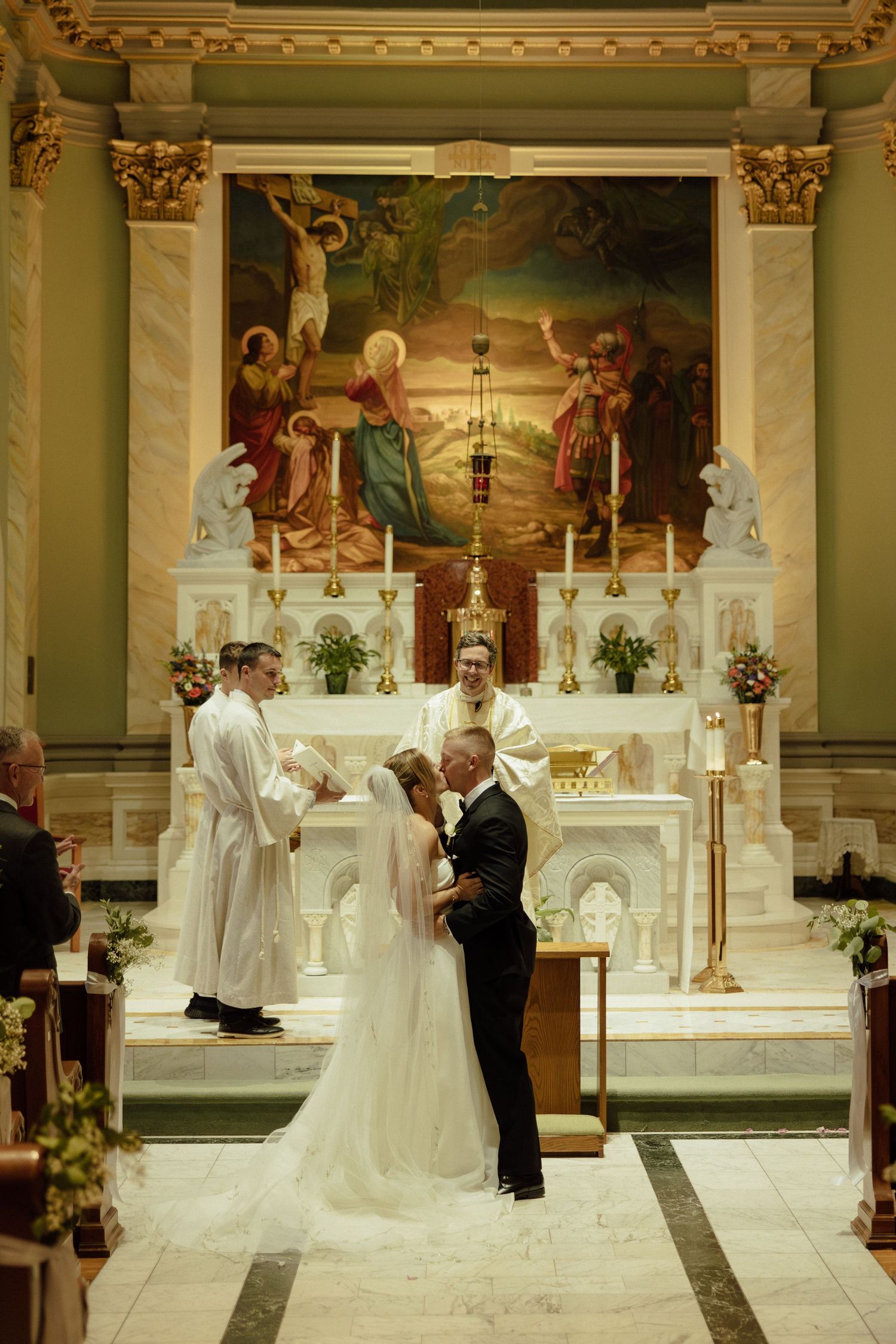 Traditional Catholic church wedding ceremony with white altar and religious artwork in background.