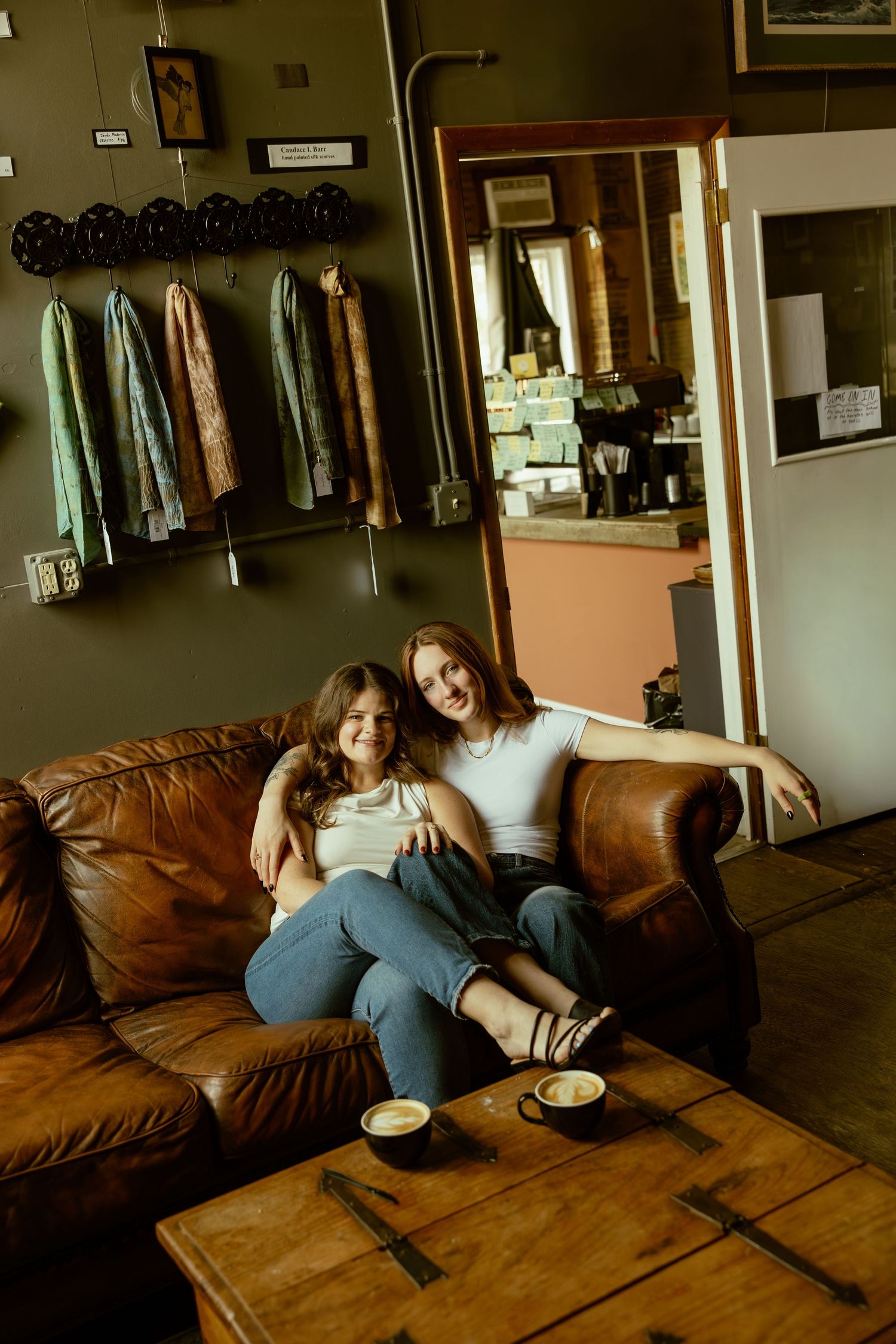 People lounging together on a leather sofa in a casual retail space with framed art and clothing on display.