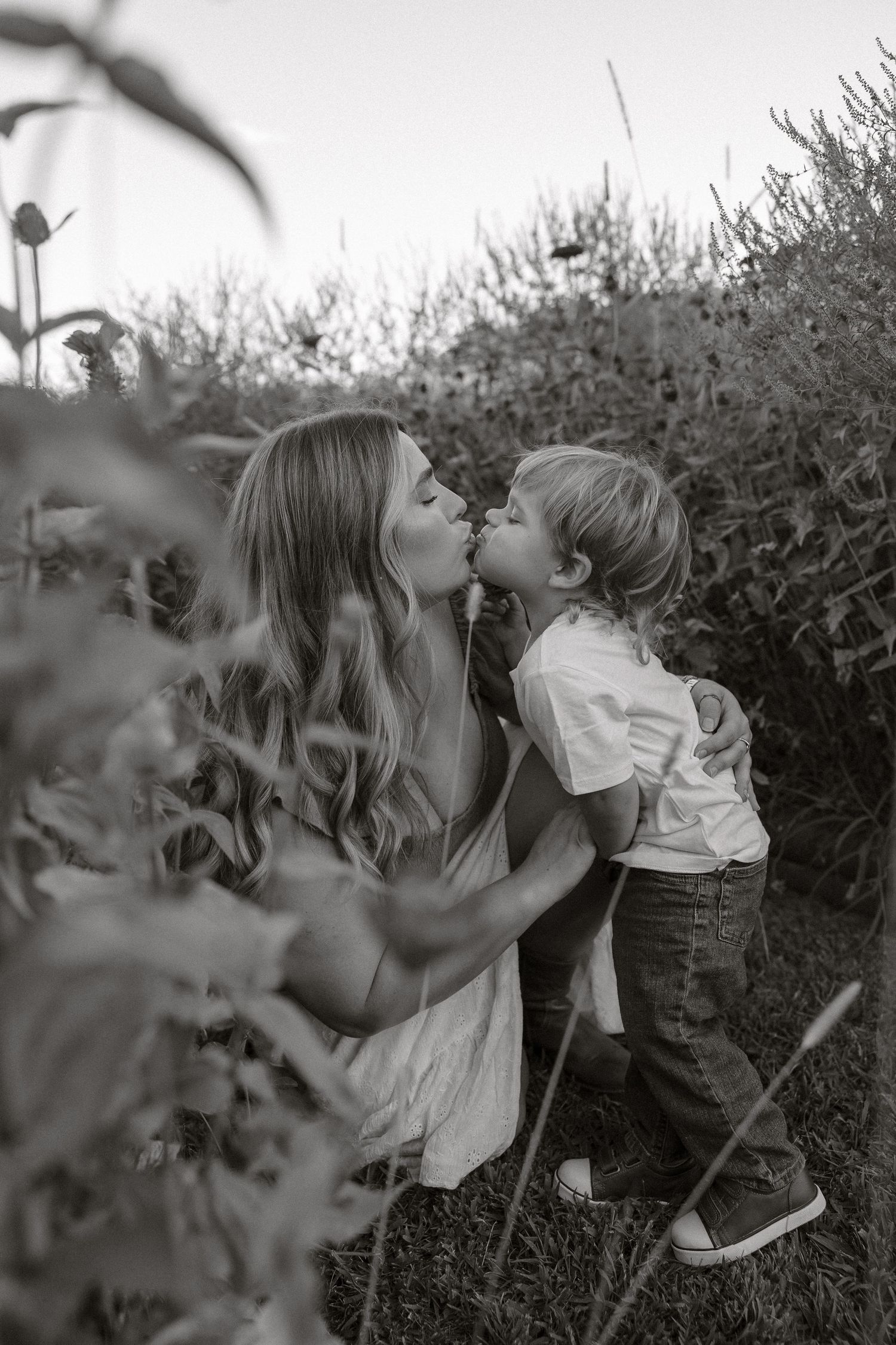 A black and white photo series showing two children sharing a sweet kiss through garden foliage.