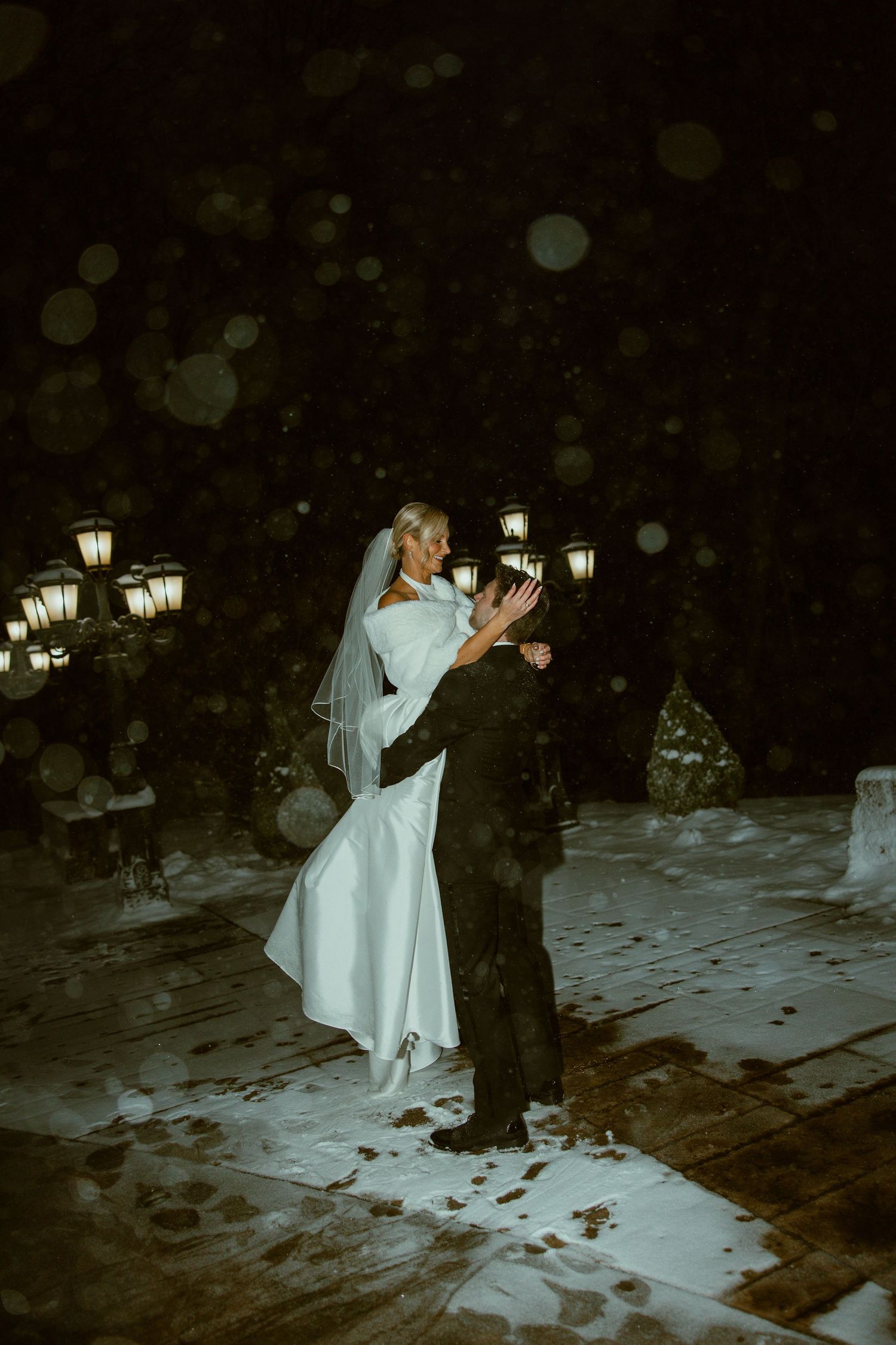 A couple shares a romantic dance under lantern lighting at a nighttime outdoor wedding celebration.