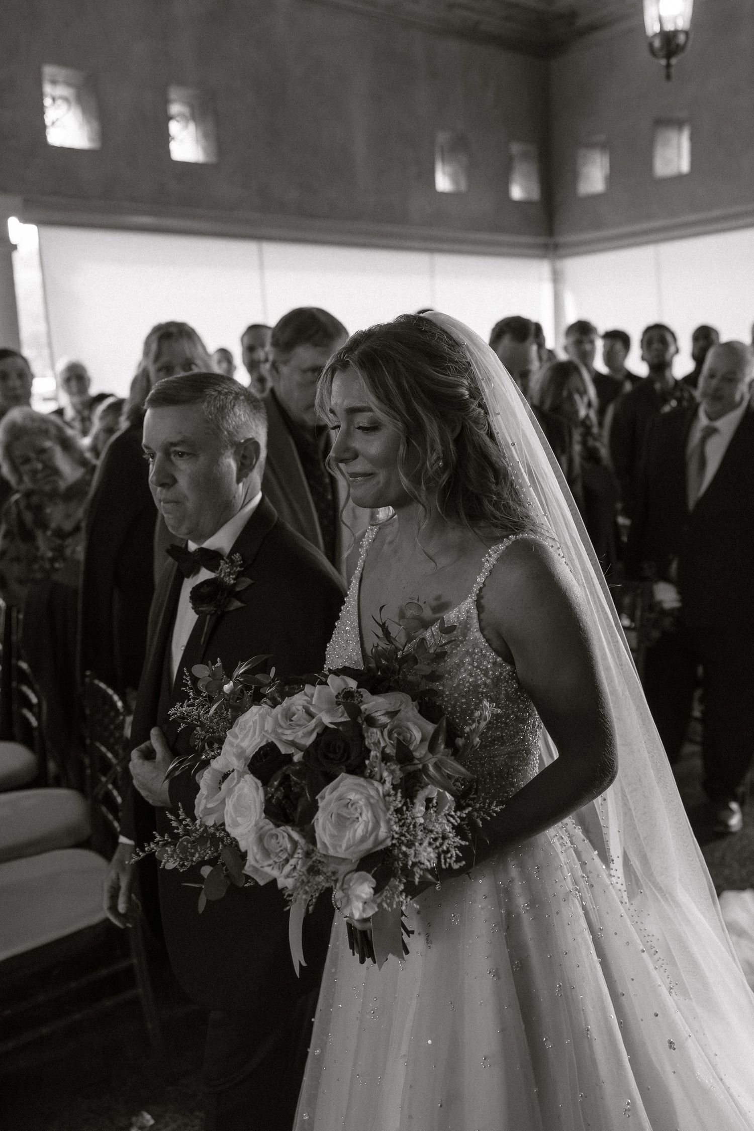 Black and white wedding ceremony photos showing guests and floral arrangements in an indoor venue.