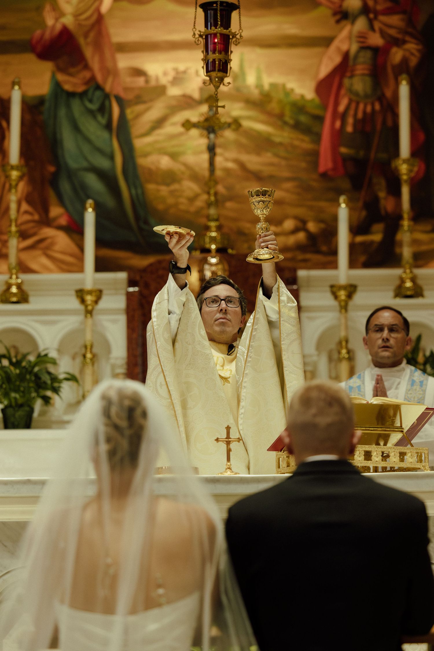 Wedding ceremony taking place in an ornate church with stained glass windows and candles.