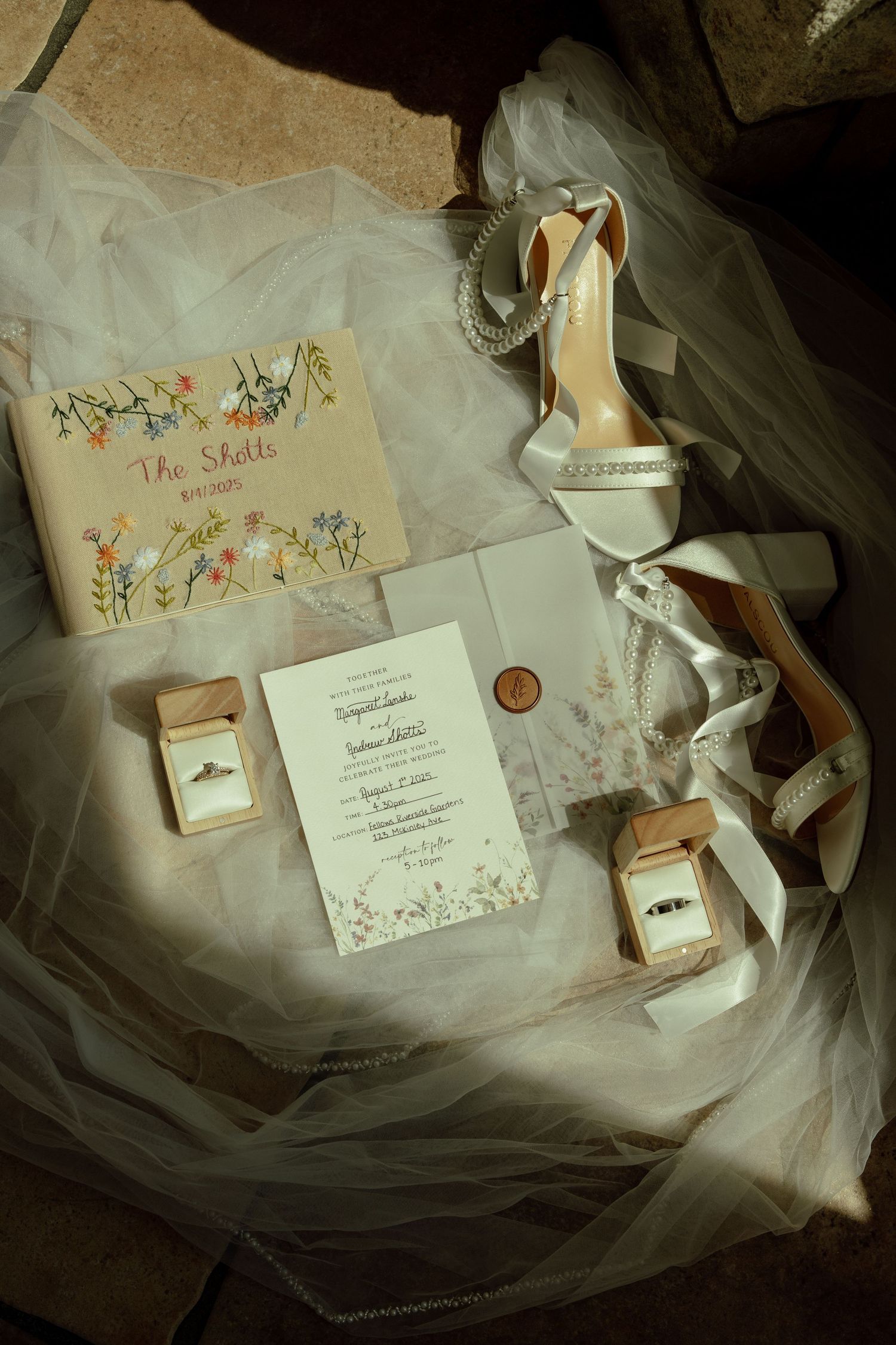 Wedding details including invitations, shoes, and floral stationery arranged on delicate tulle fabric.