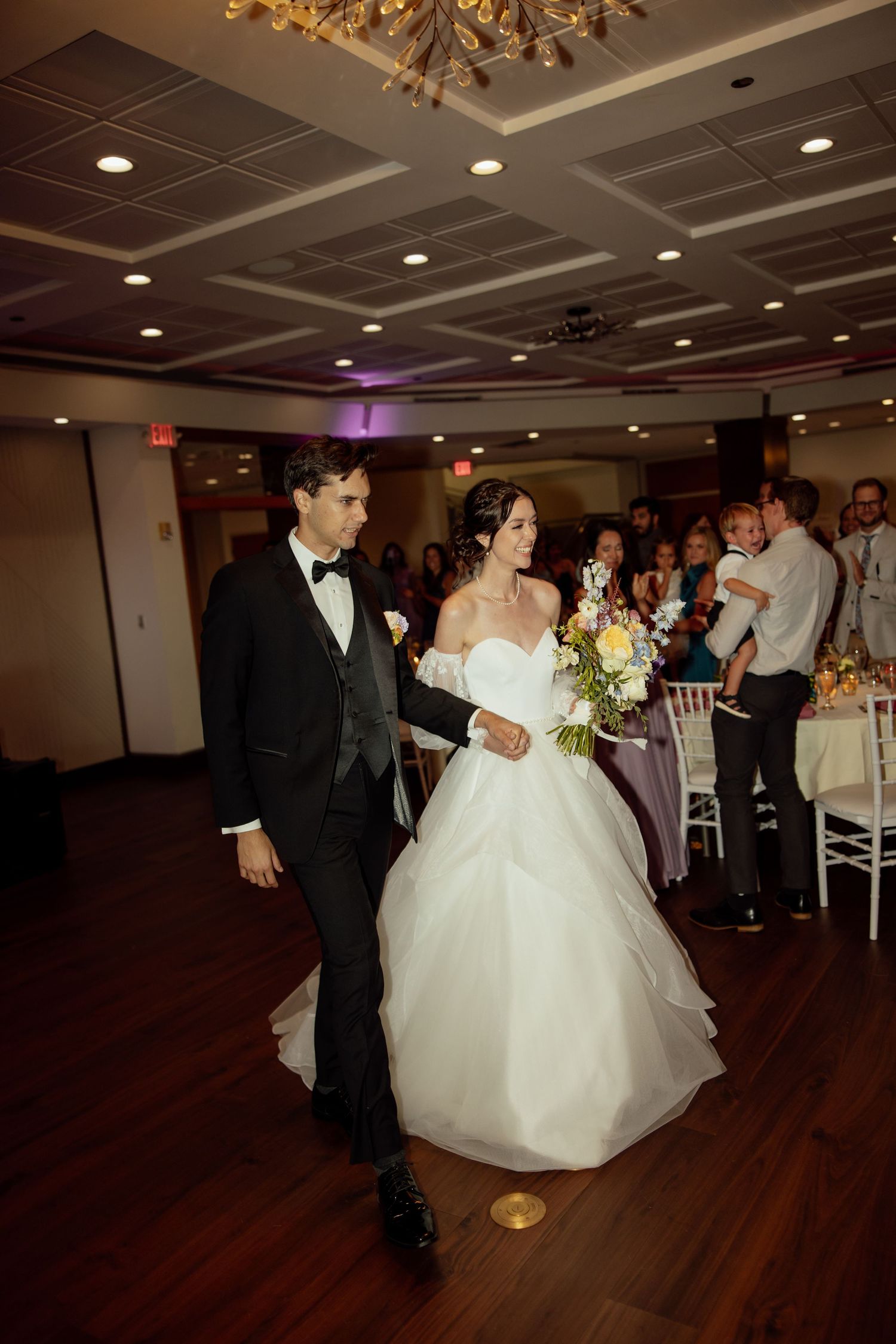 A couple dances together during their first dance at a wedding reception on a wooden dance floor.
