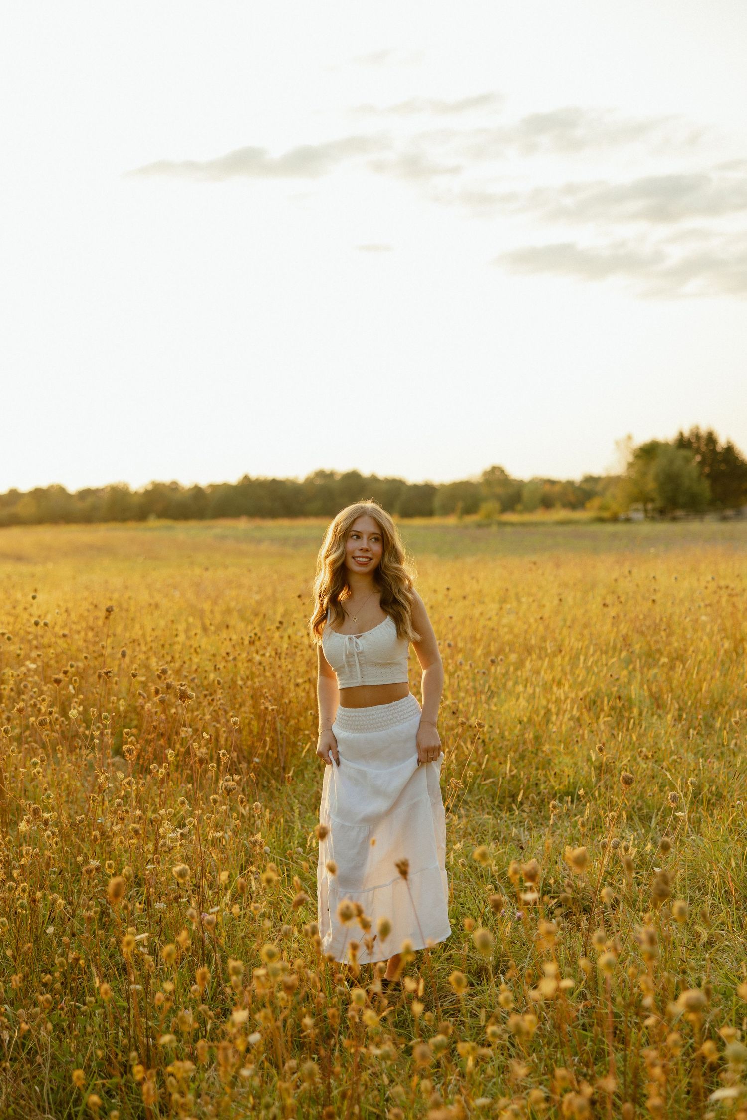 Person in white dress twirling through a sunlit field of wildflowers at sunset.