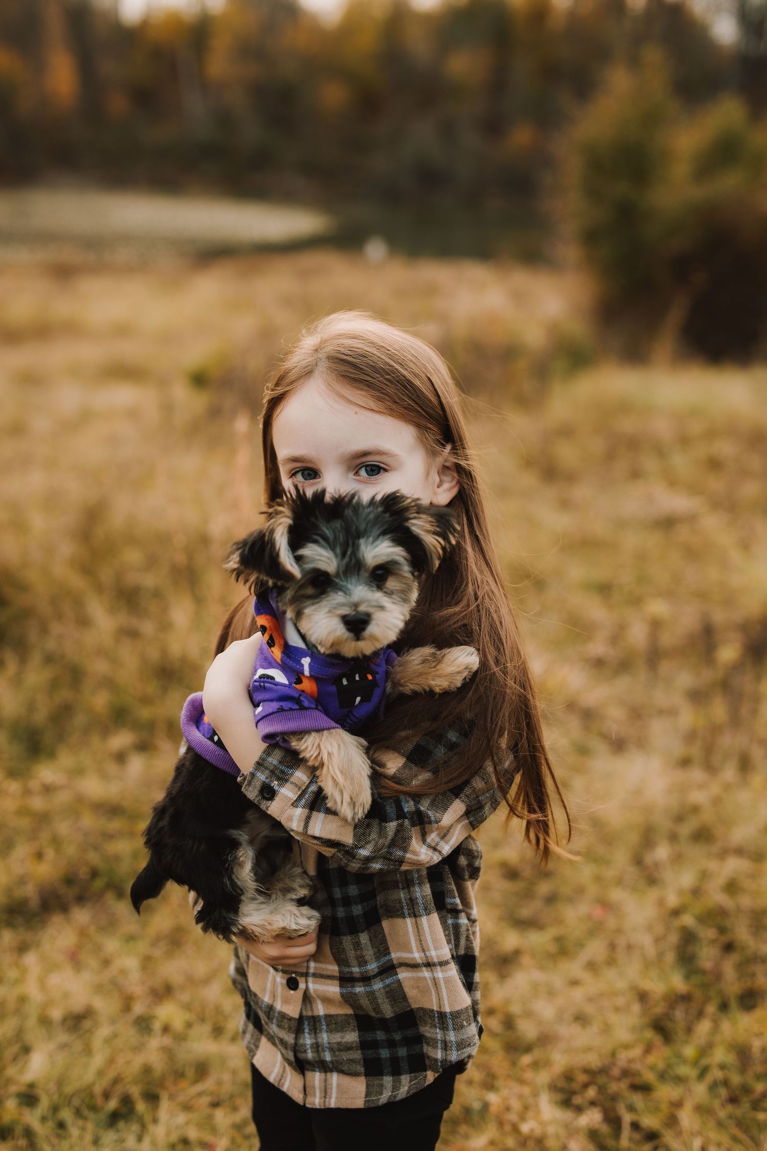 A young child holding a small black and white puppy wearing a blue bandana.