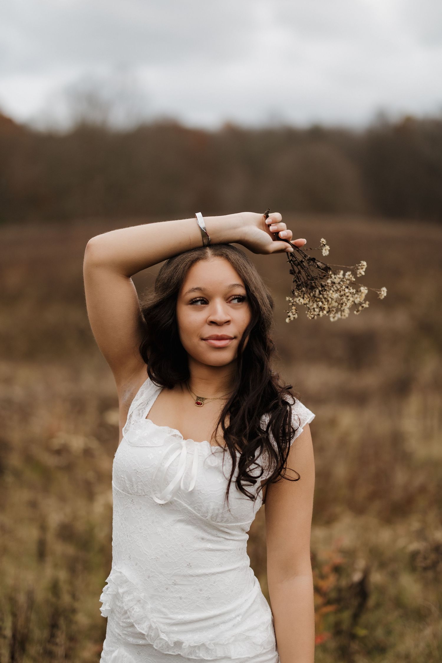 A portrait in a field shows someone wearing a white dress with dried flowers in the background.