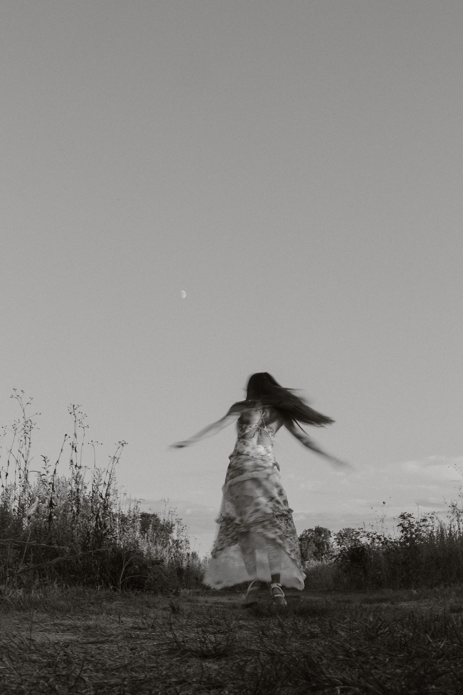 A series of black and white photographs showing a figure in white dress twirling and moving through a field against the sky.
