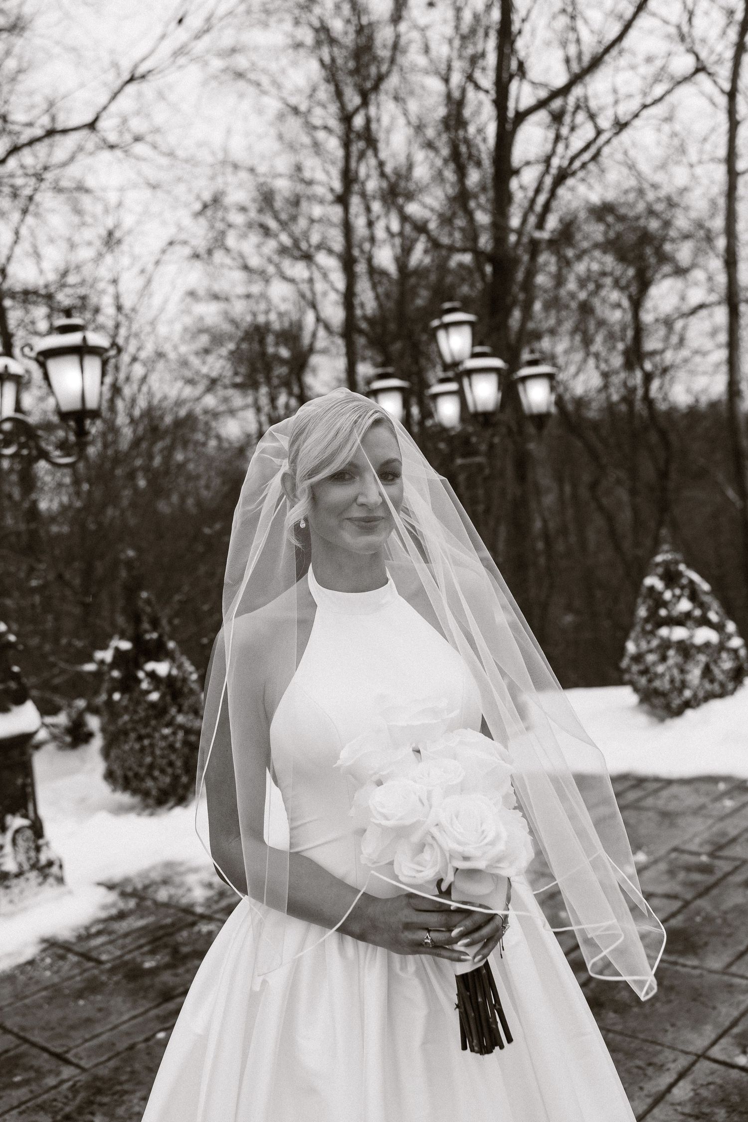 Elegant winter bridal portraits in snow with delicate veil and white dress details.