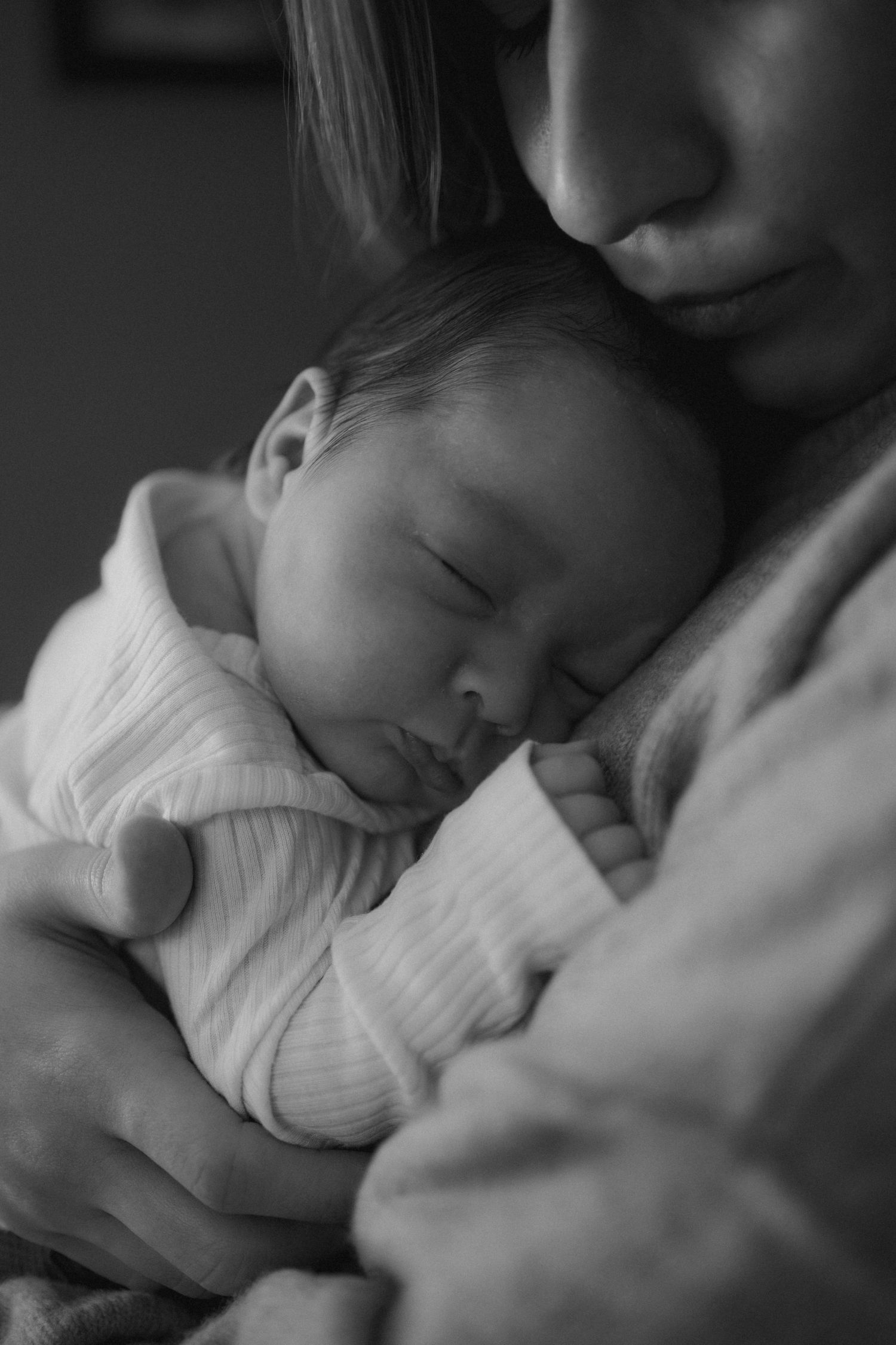 An intimate black and white portrait of a sleeping newborn being held close.
