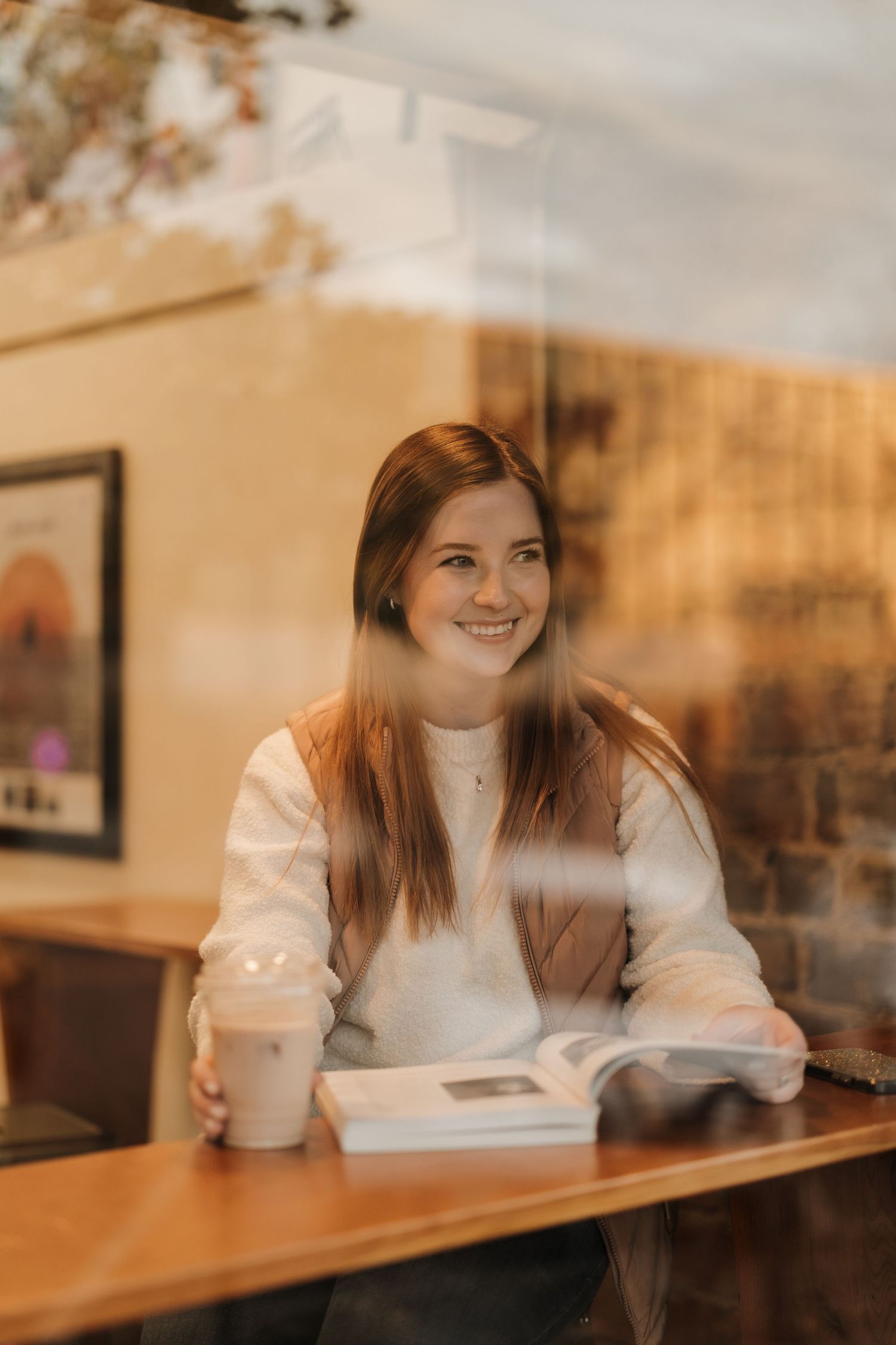 Person enjoying coffee and reading at a cozy cafe with warm lighting and framed artwork on the wall.