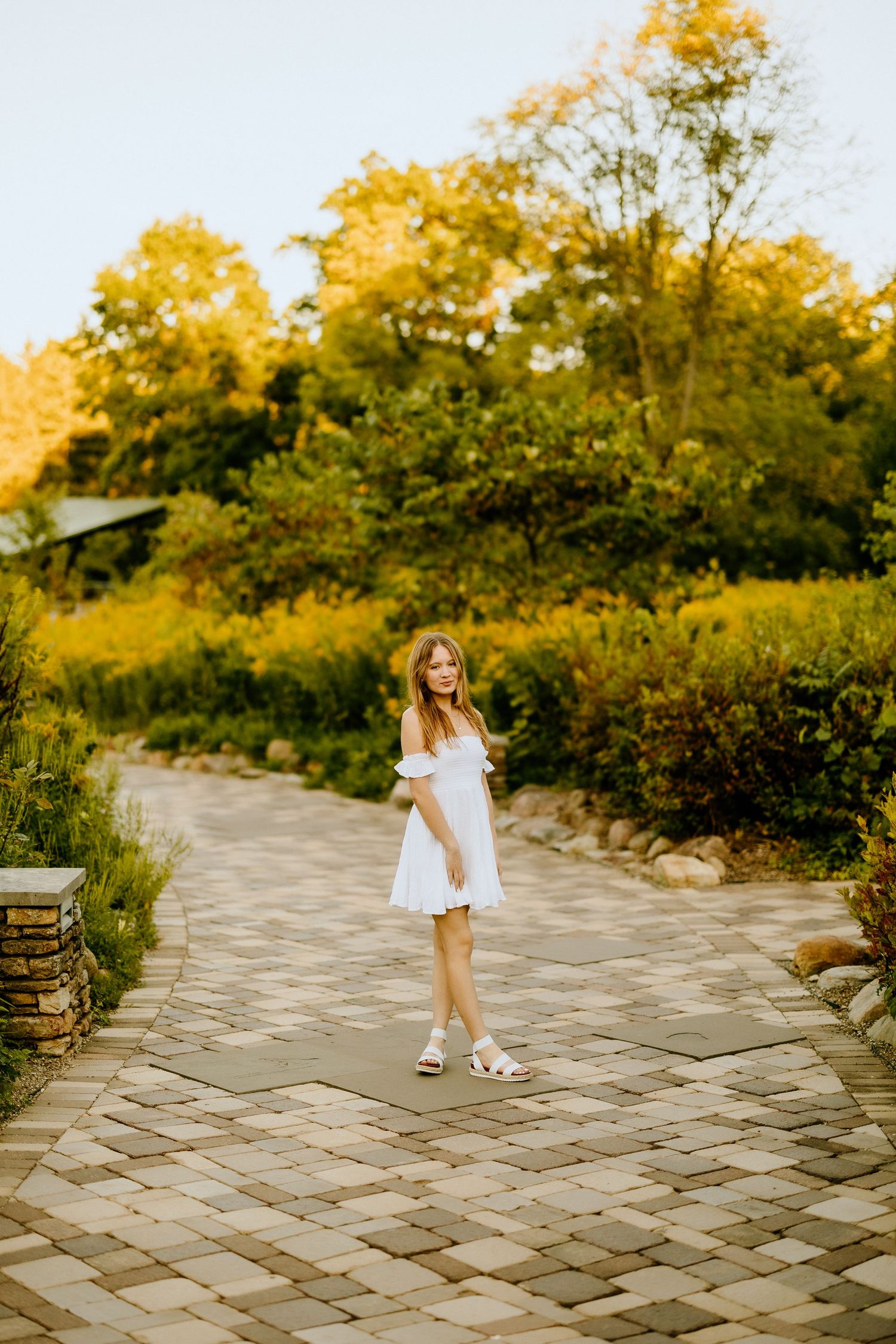 A flowing white dress stands out against a winding stone path surrounded by autumn foliage.
