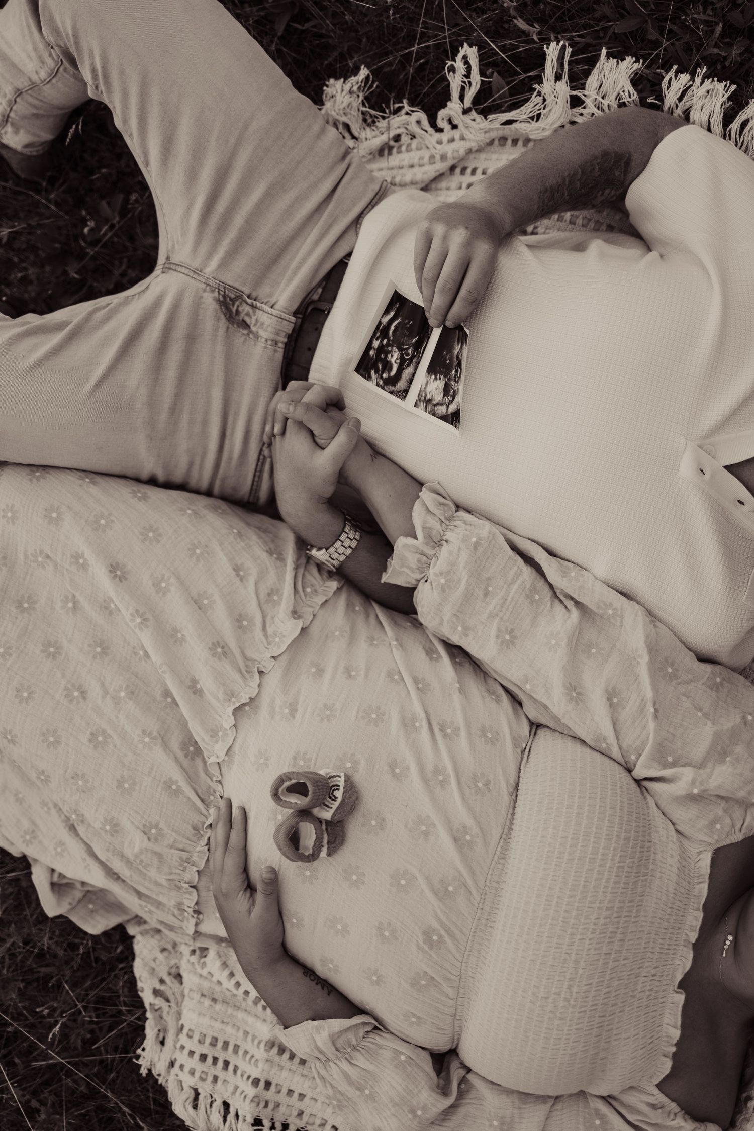 A black and white photo showing someone lying down holding ultrasound photos on a patterned blanket.