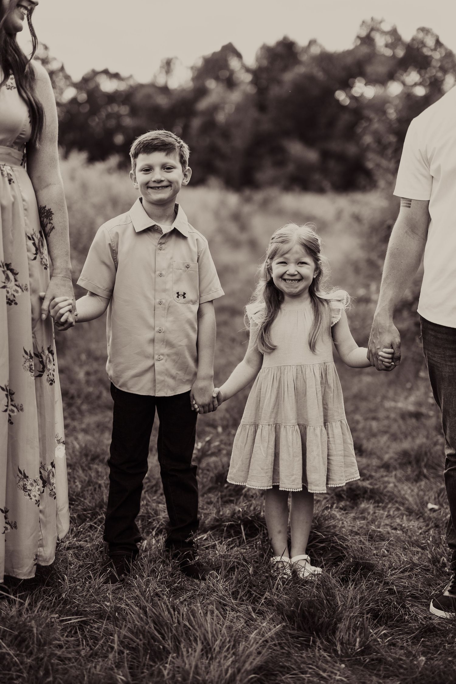 Black and white portrait of siblings holding hands with parents in an outdoor field setting.