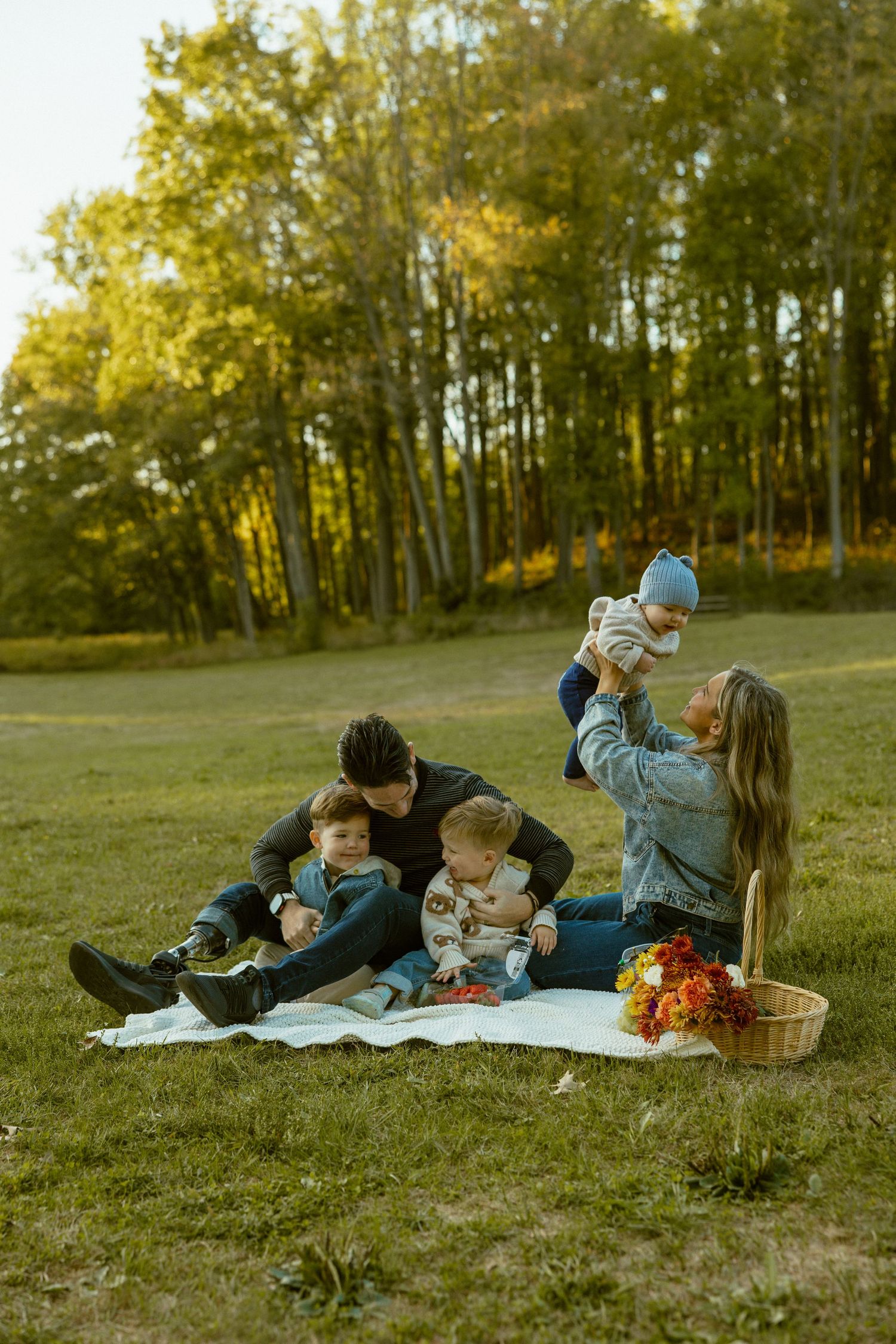 A family enjoys a cozy autumn picnic on a blanket in a sunlit meadow with golden trees in the background.