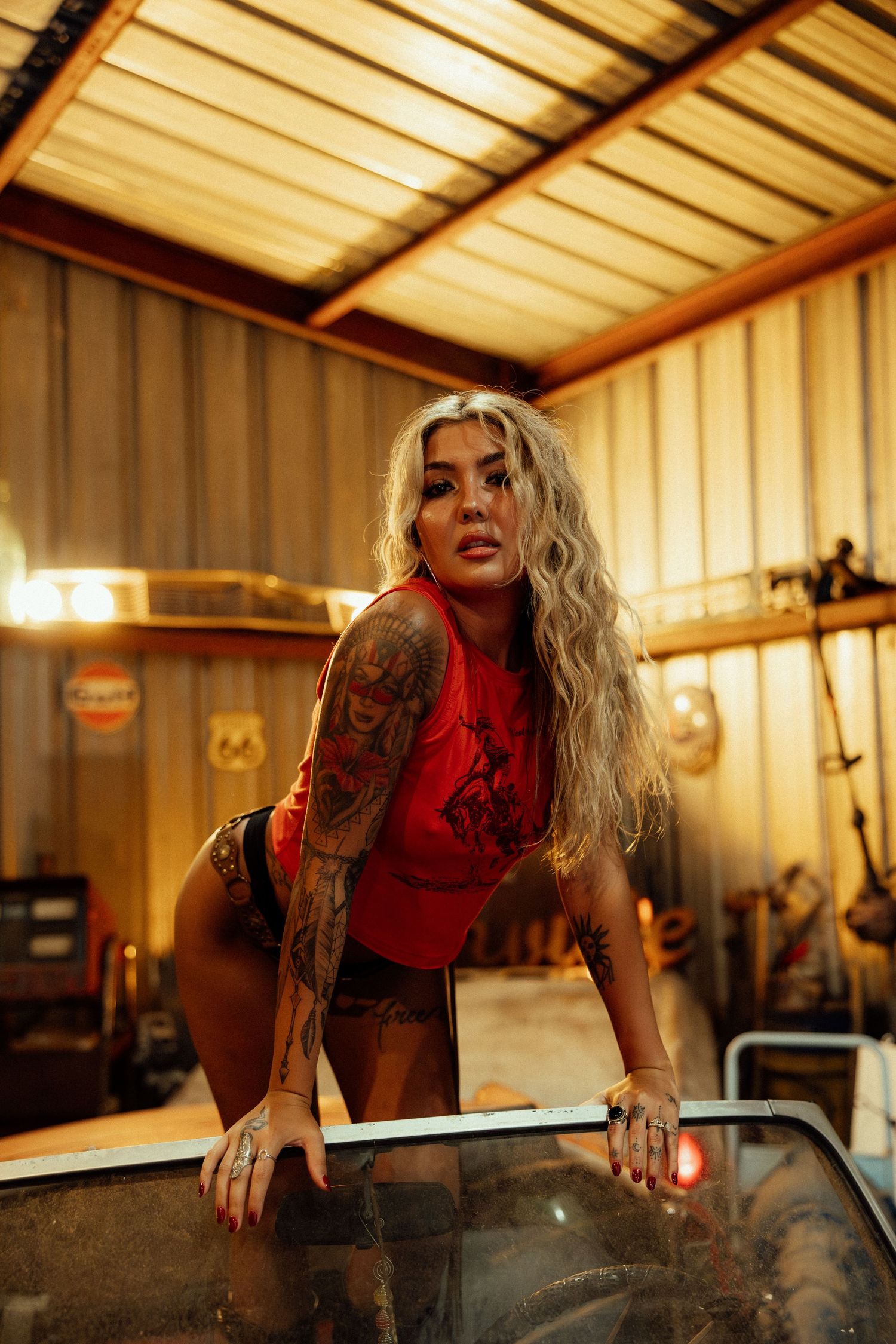 Woman in red top leaning over and reaching inside a rustic indoor workshop setting.