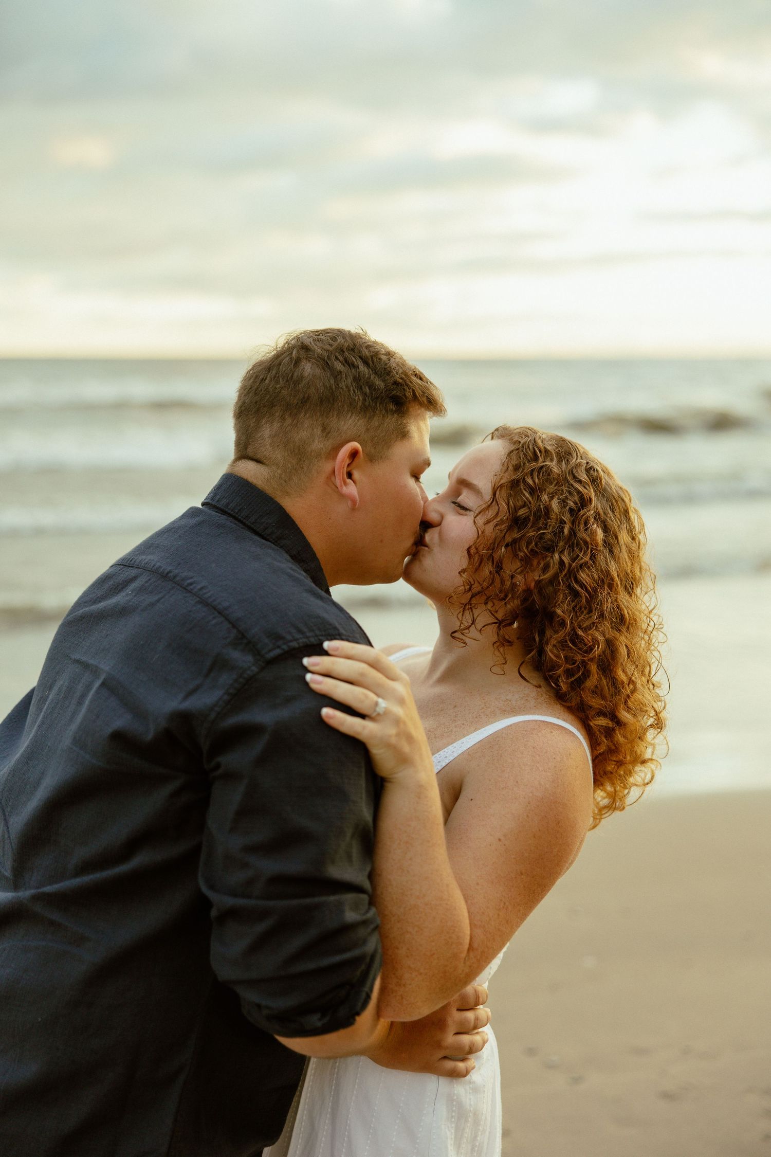 A romantic couple sharing a tender kiss on a misty beach at sunset.