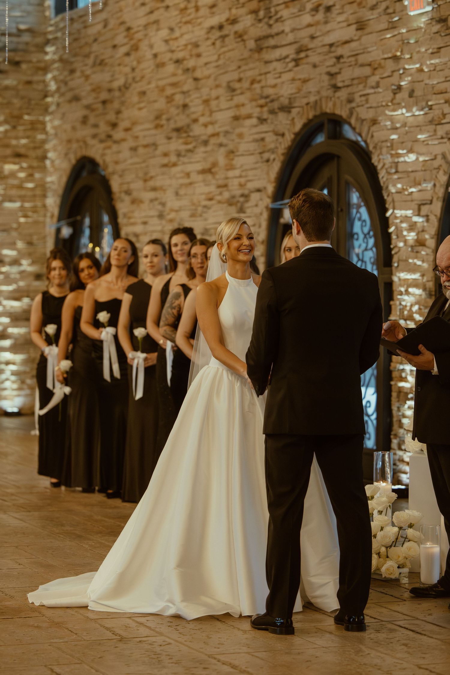 Wedding party poses inside a stone-walled venue with elegant lighting and arched details.