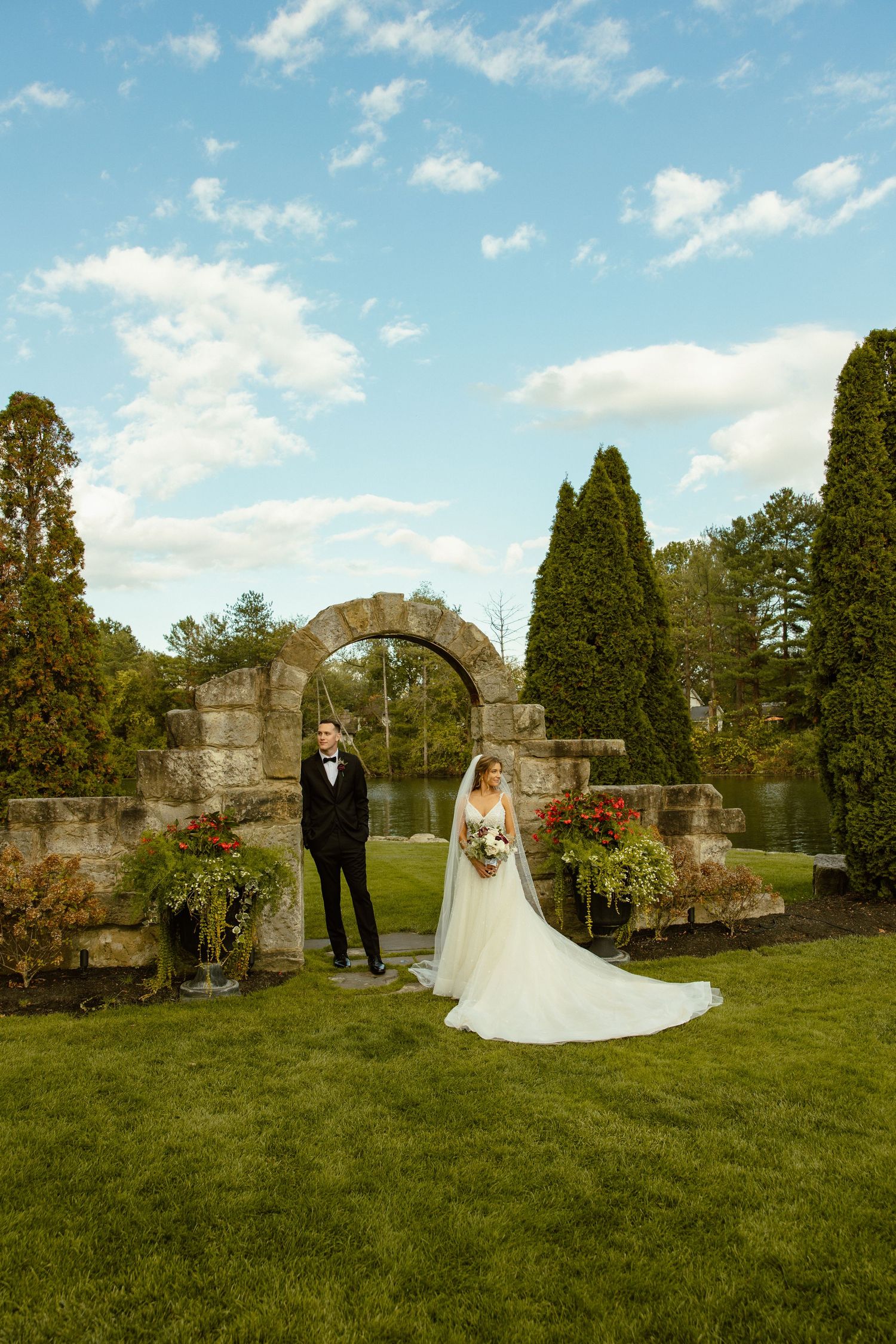 A wedding couple poses for romantic portraits in front of stone ruins surrounded by cypress trees on a sunny day.