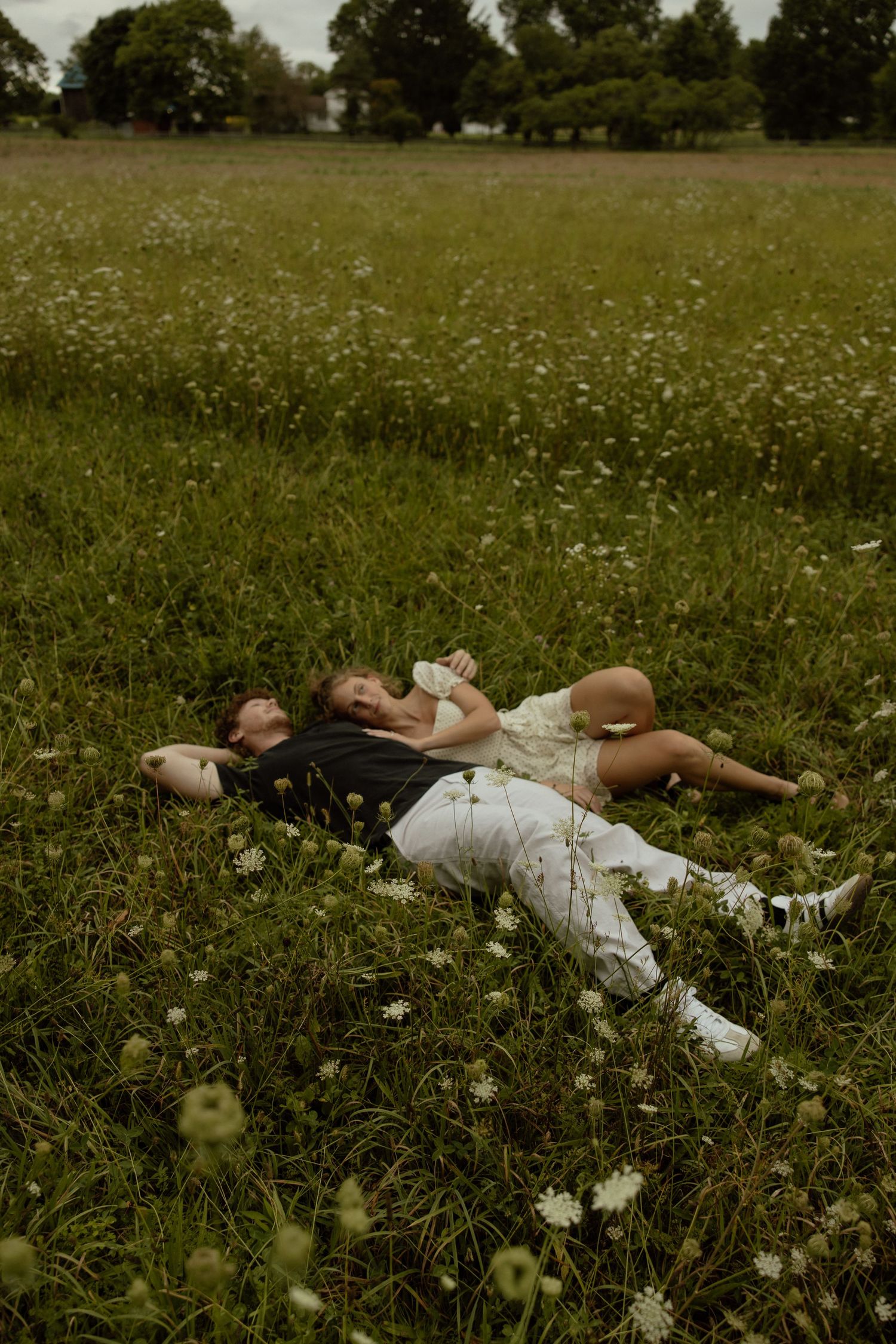 People lying in a peaceful meadow filled with white wildflowers and tall grass on a summer day.