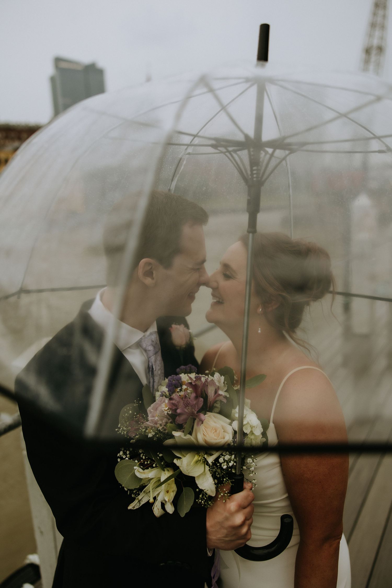 Intimate wedding moment captured under a clear umbrella on an overcast day.