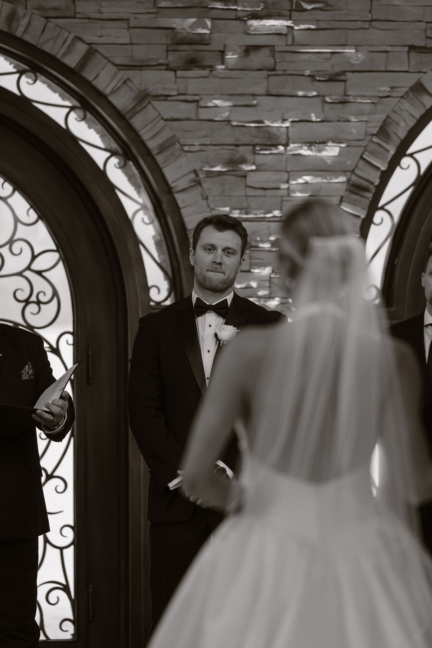 A bride in a white wedding dress walking through an ornate stone archway.