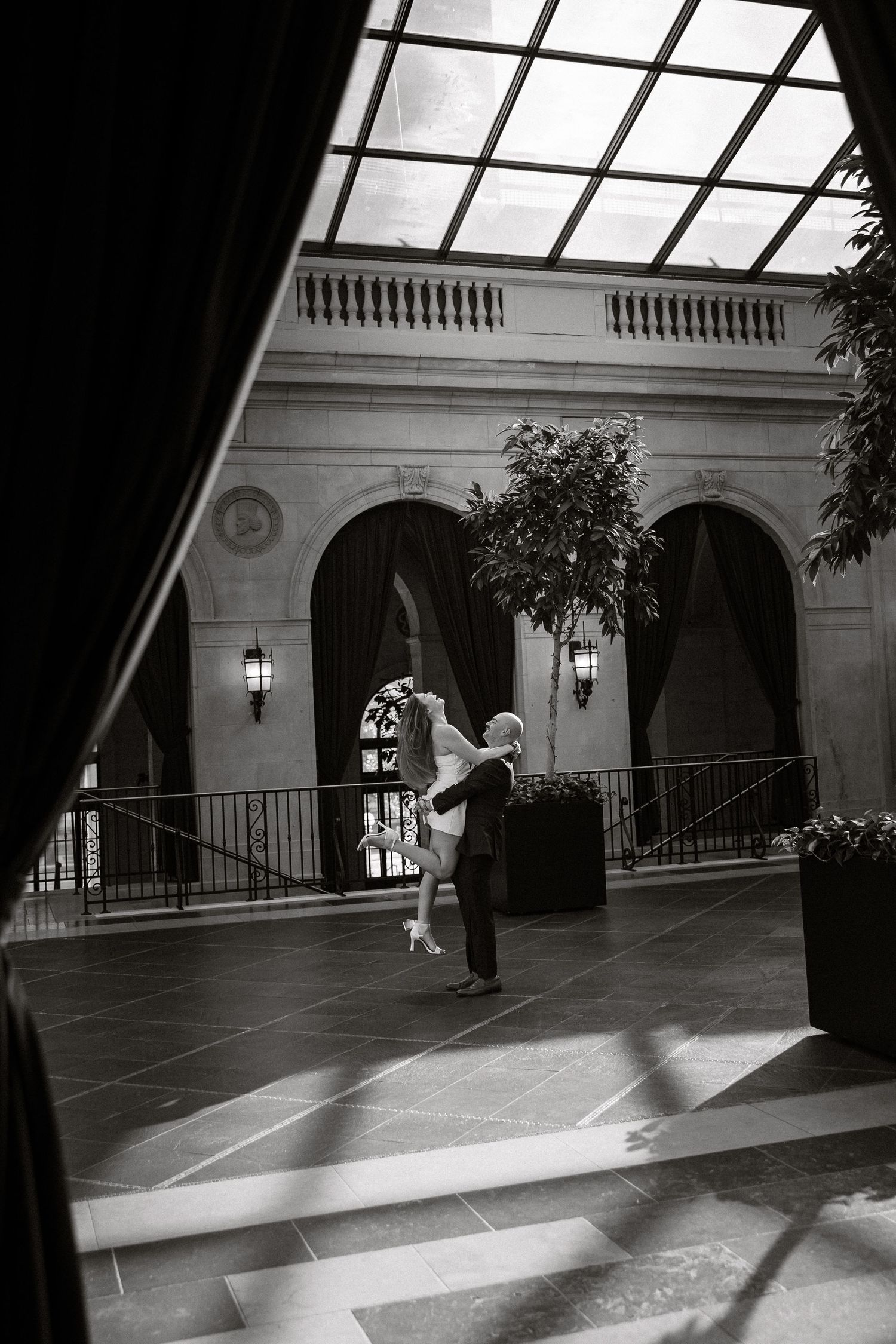 A couple dances intimately in a grand arched hallway with dramatic lighting and architectural details.
