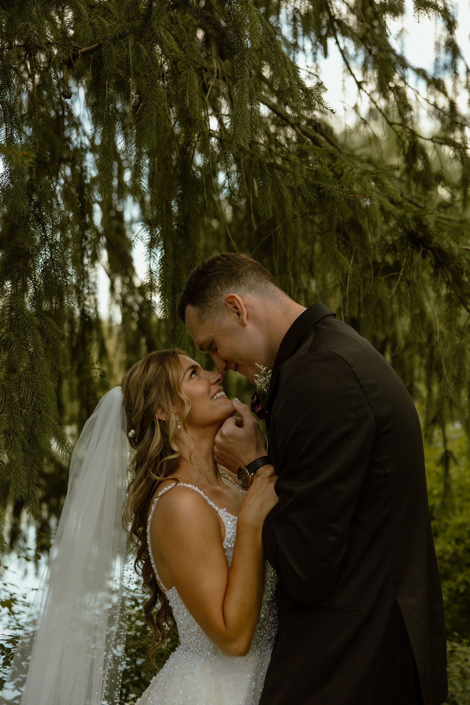 A romantic wedding moment captured under willow trees with the bride in a white gown and veil.