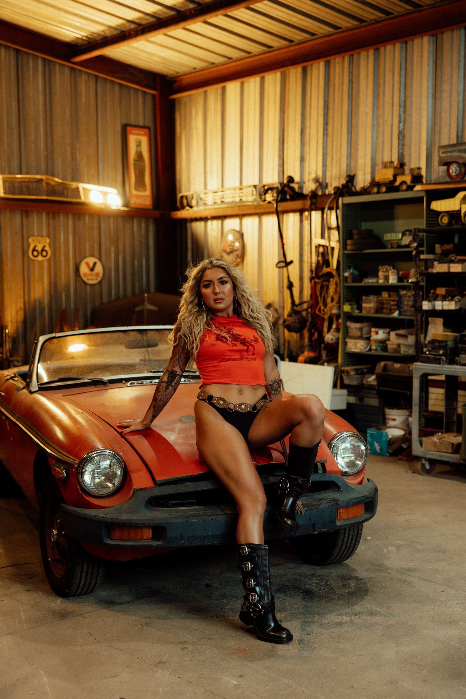 A classic red sports car parked inside a rustic garage workshop with tools and equipment on shelves.