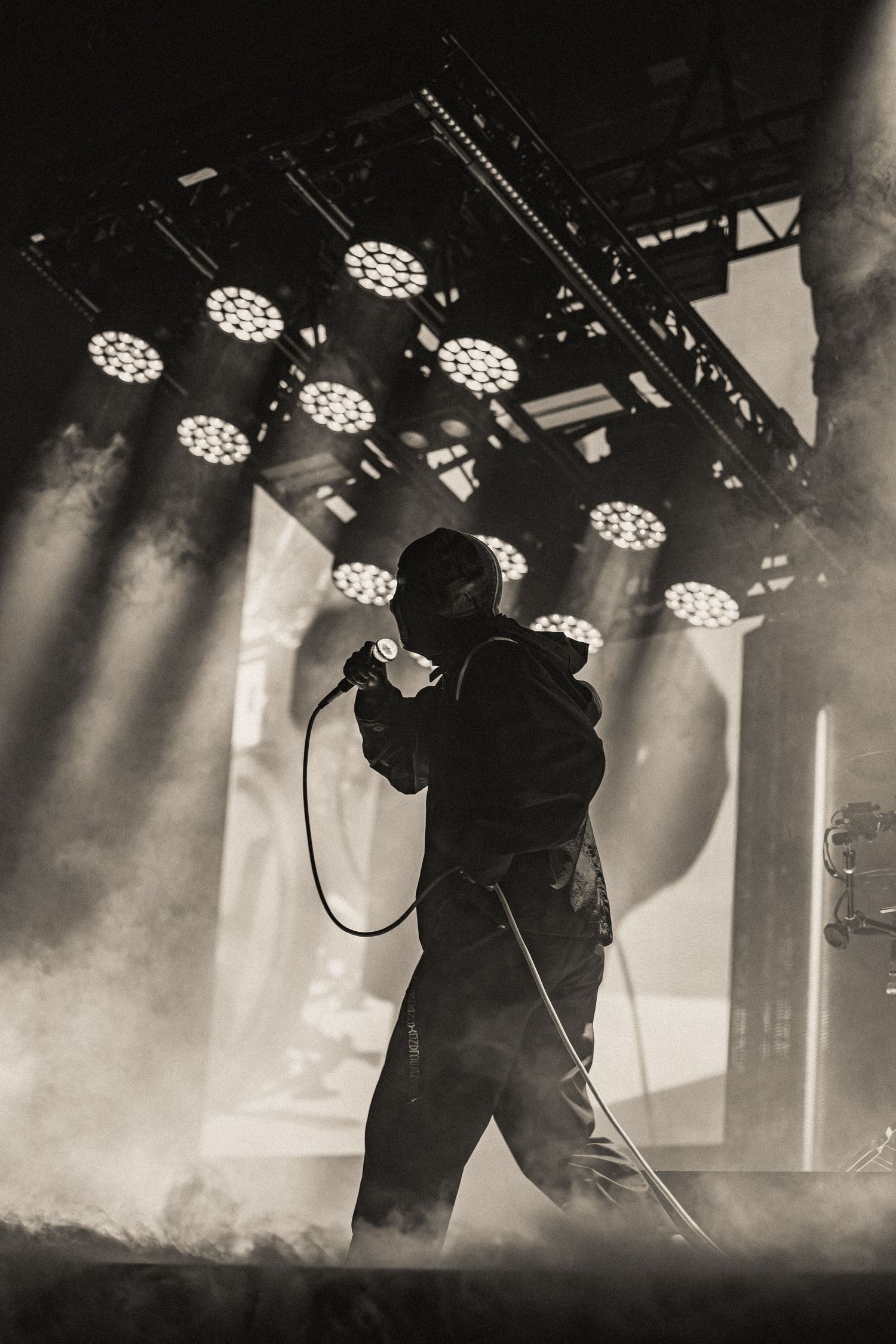 Silhouette of performer on smoky stage with LED light array overhead in black and white.
